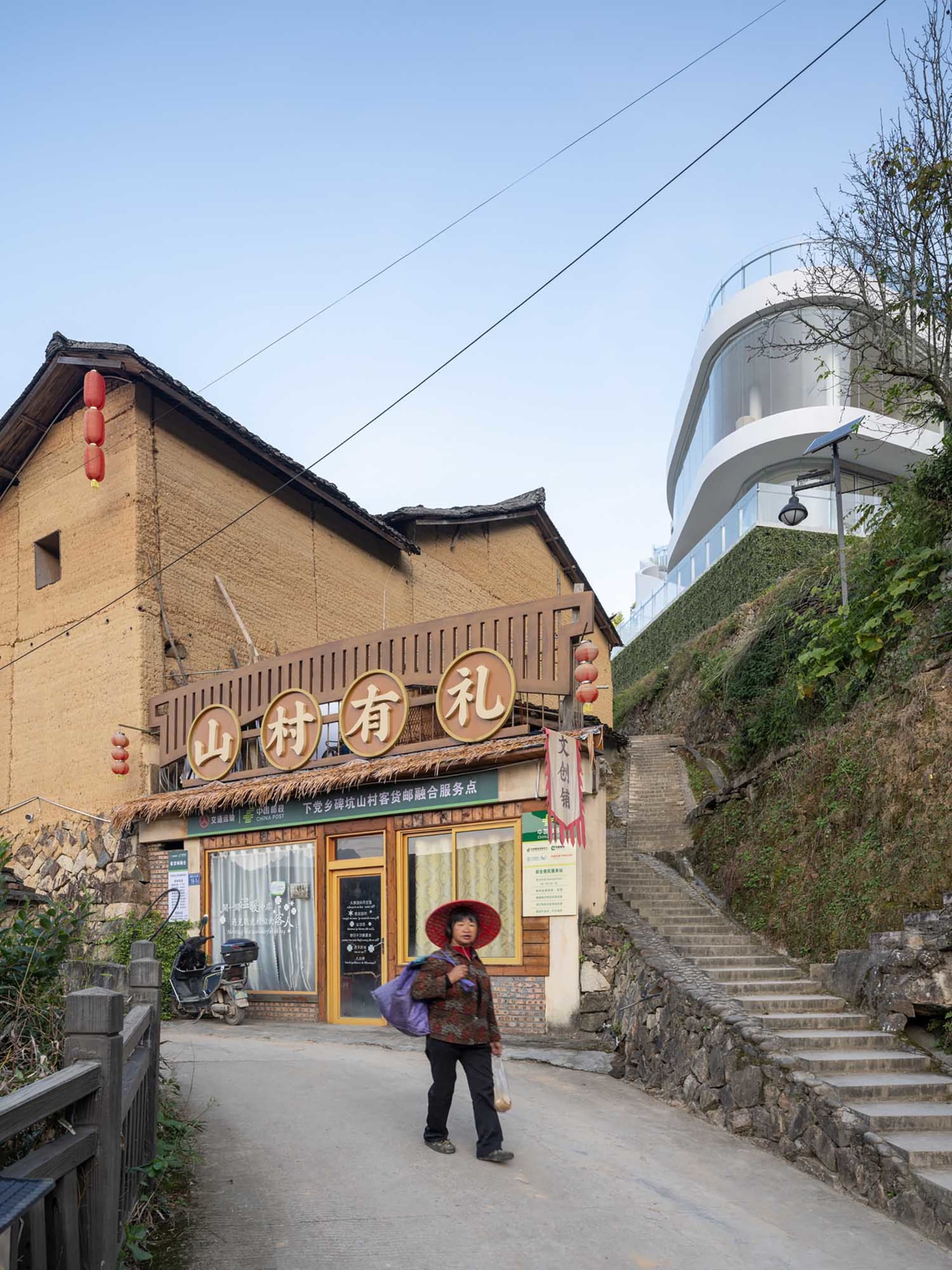 A woman walks down stairs in front of a restaurant with Chinese lettering and a blend of traditional and modern architecture in an urban setting