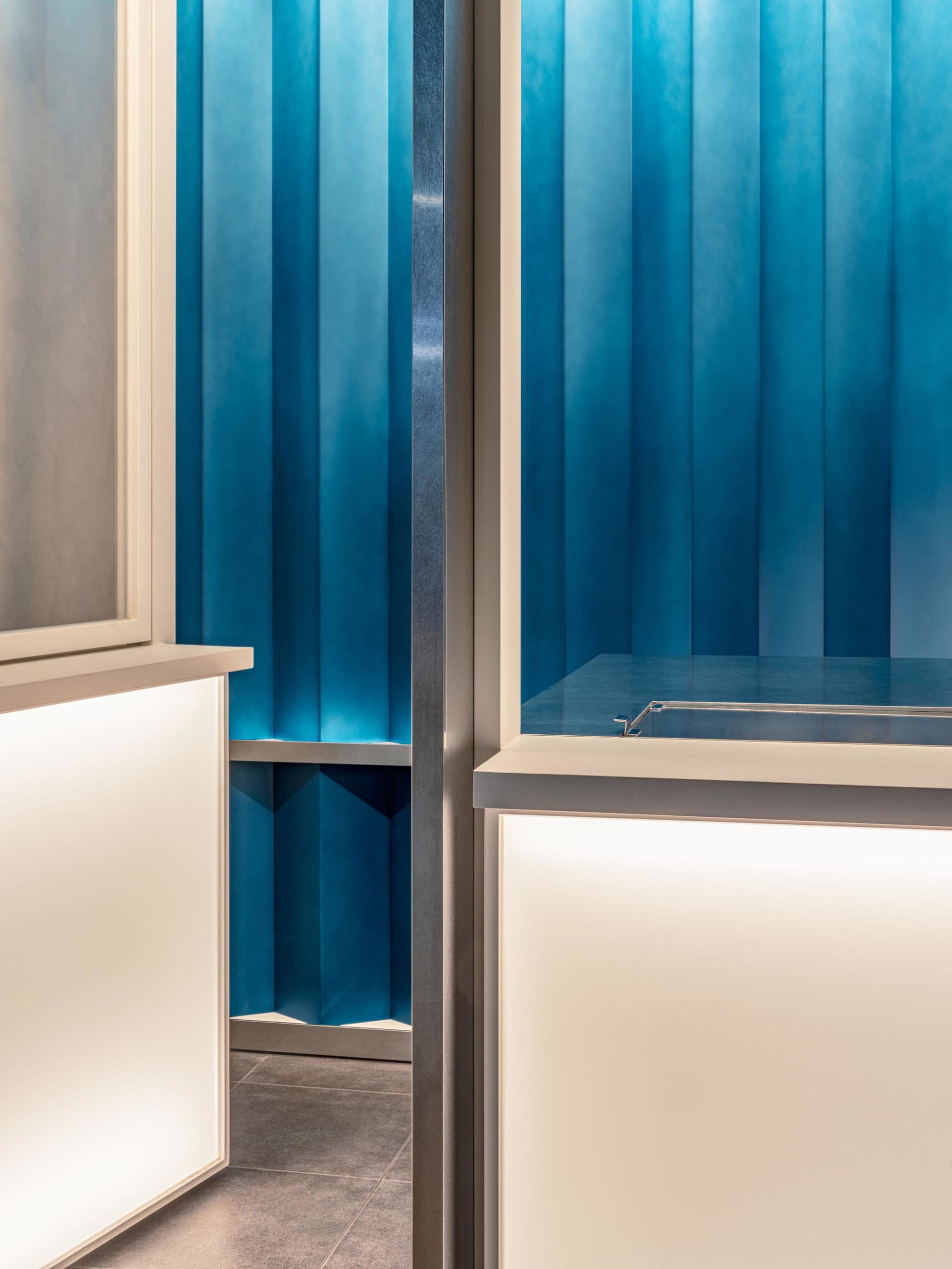 A modern kitchen with a blue tinted glass wall behind a countertop, flanked by two doors, with blue walls and a marble countertop