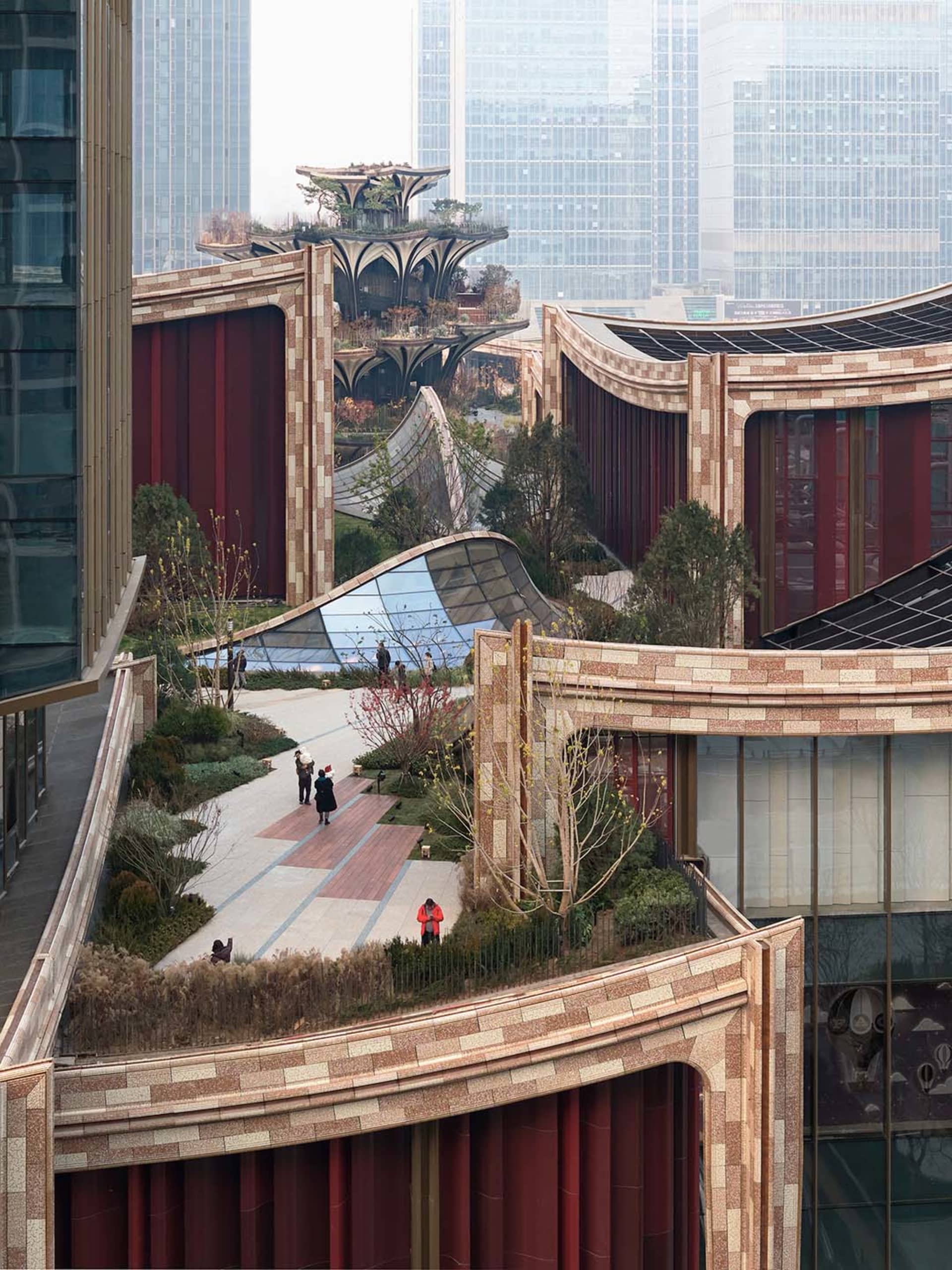 A bustling city center with a large building featuring red brick and glass surfaces, surrounded by people going about their daily activities