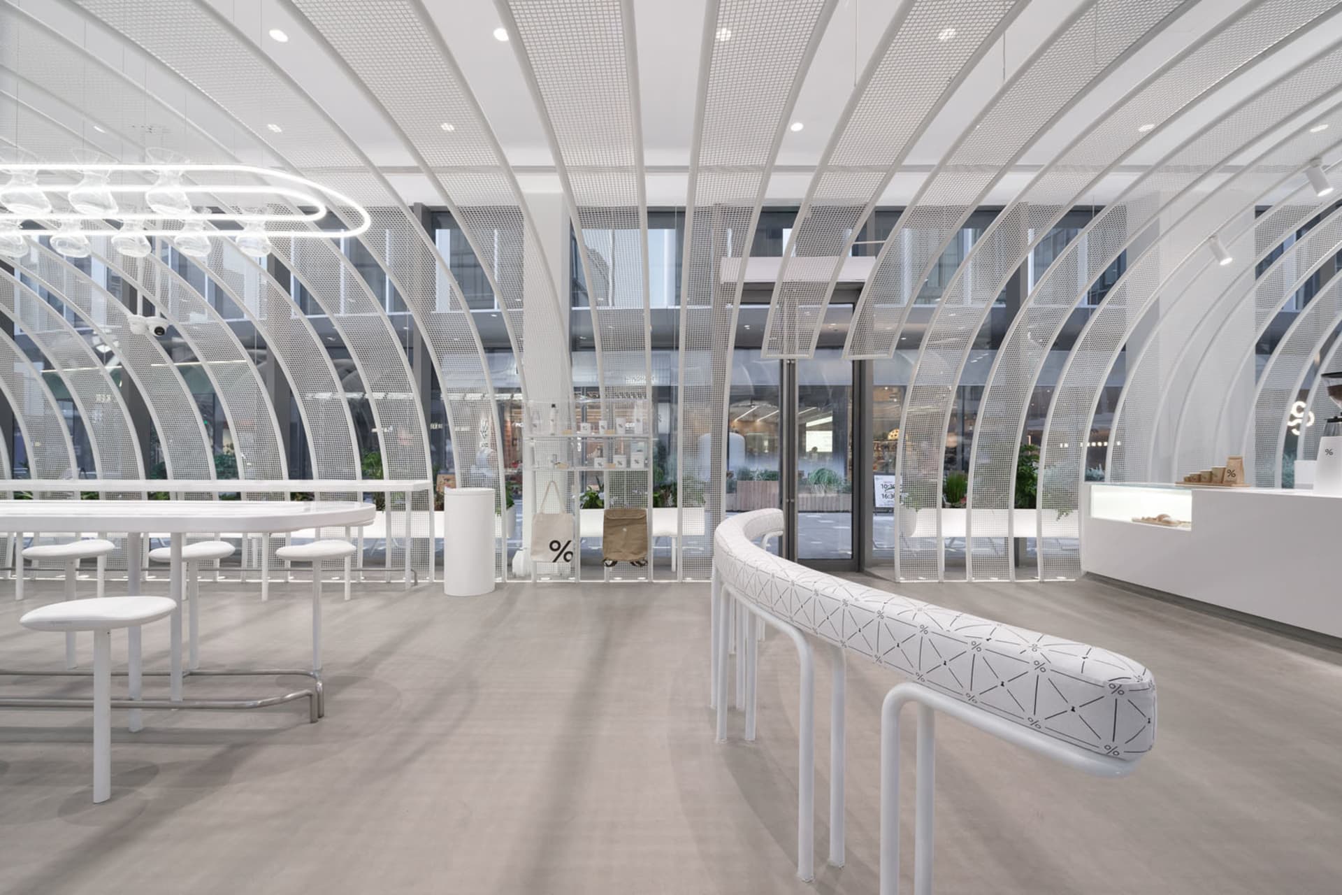 Bright and inviting open space with white walls, benches, tables, chairs, and potted plants, with natural light streaming through the windows