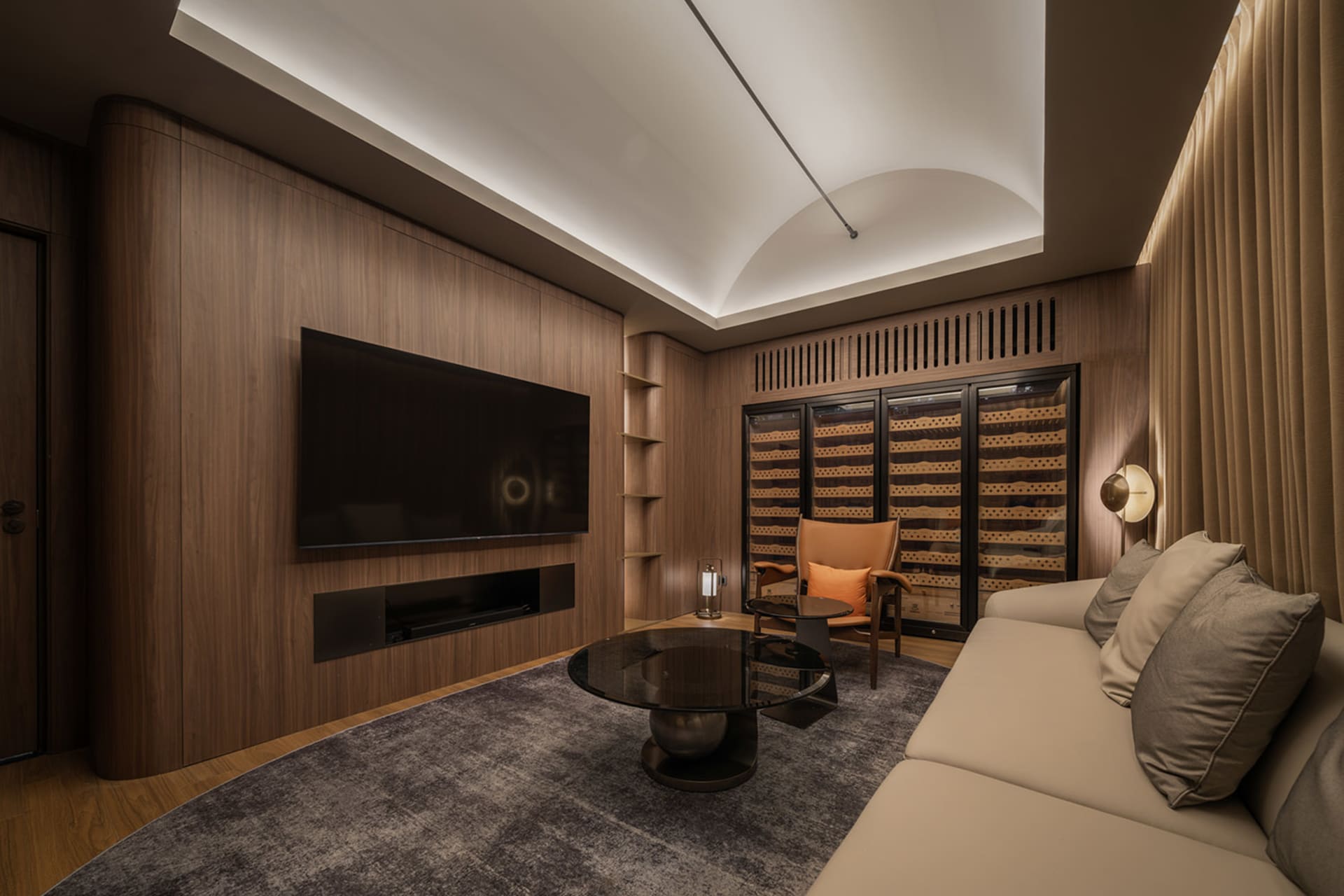 Cozy living room with wooden floors, a large flat screen TV, a fireplace, and a wine cellar, with comfortable seating and several bottles throughout