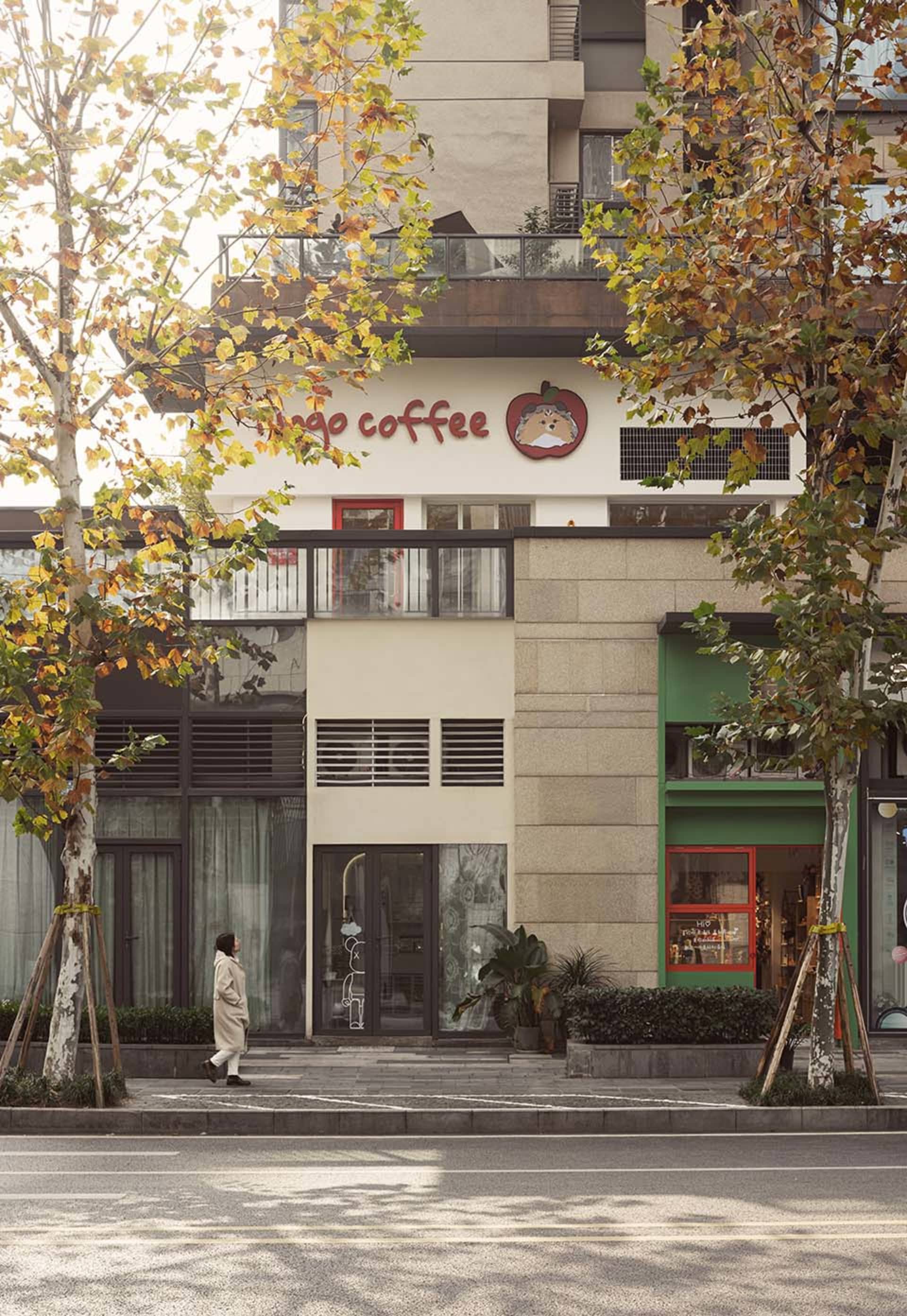 A lively urban street scene with a coffee shop on the ground floor of a green-facaded building, next to a red and white building with large windows