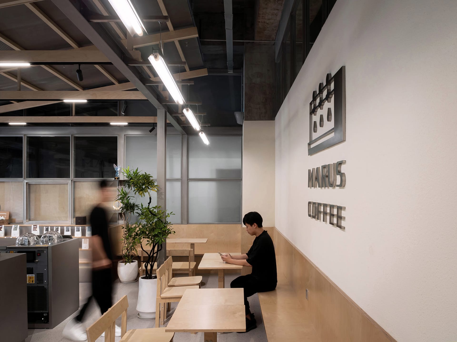 休閒室內咖啡廳場景，配有木桌椅、盆栽植物，以及一位坐在椅子上的人