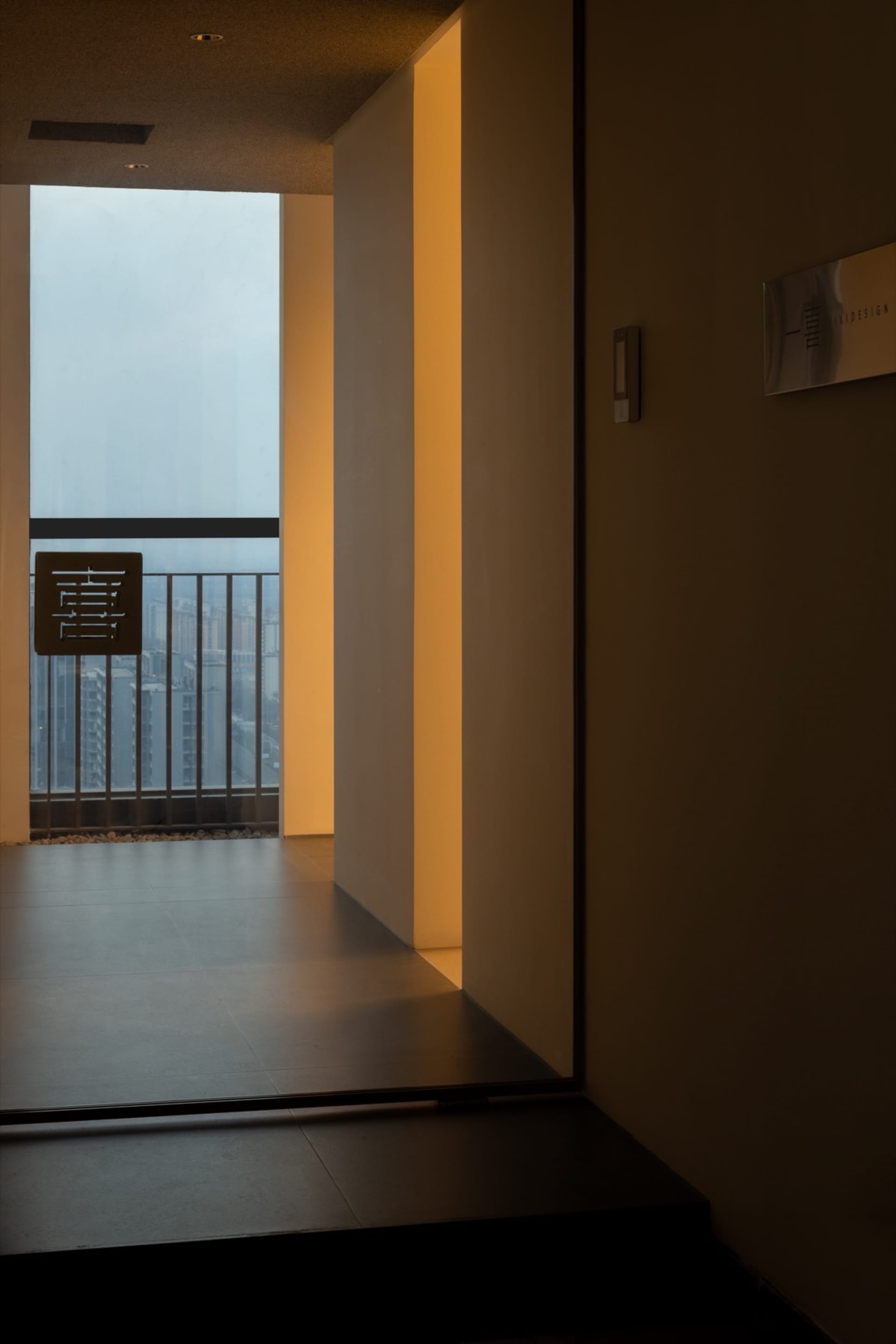 Interior view of a dimly lit room with a balcony and metal railing, visible through a window