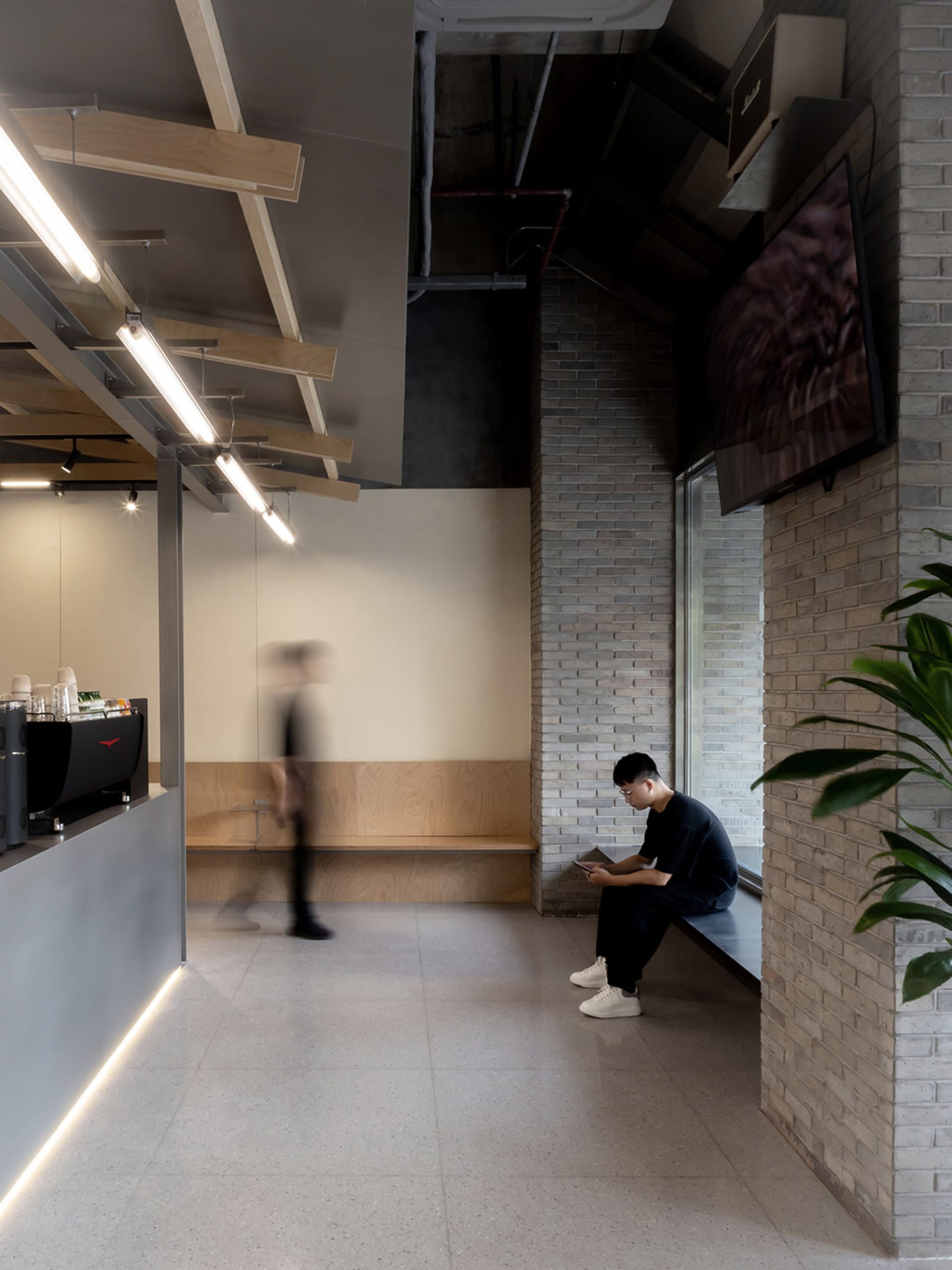 A relaxed restaurant and living area with a bench, potted plant, dining table, and chairs, featuring wood and stone materials