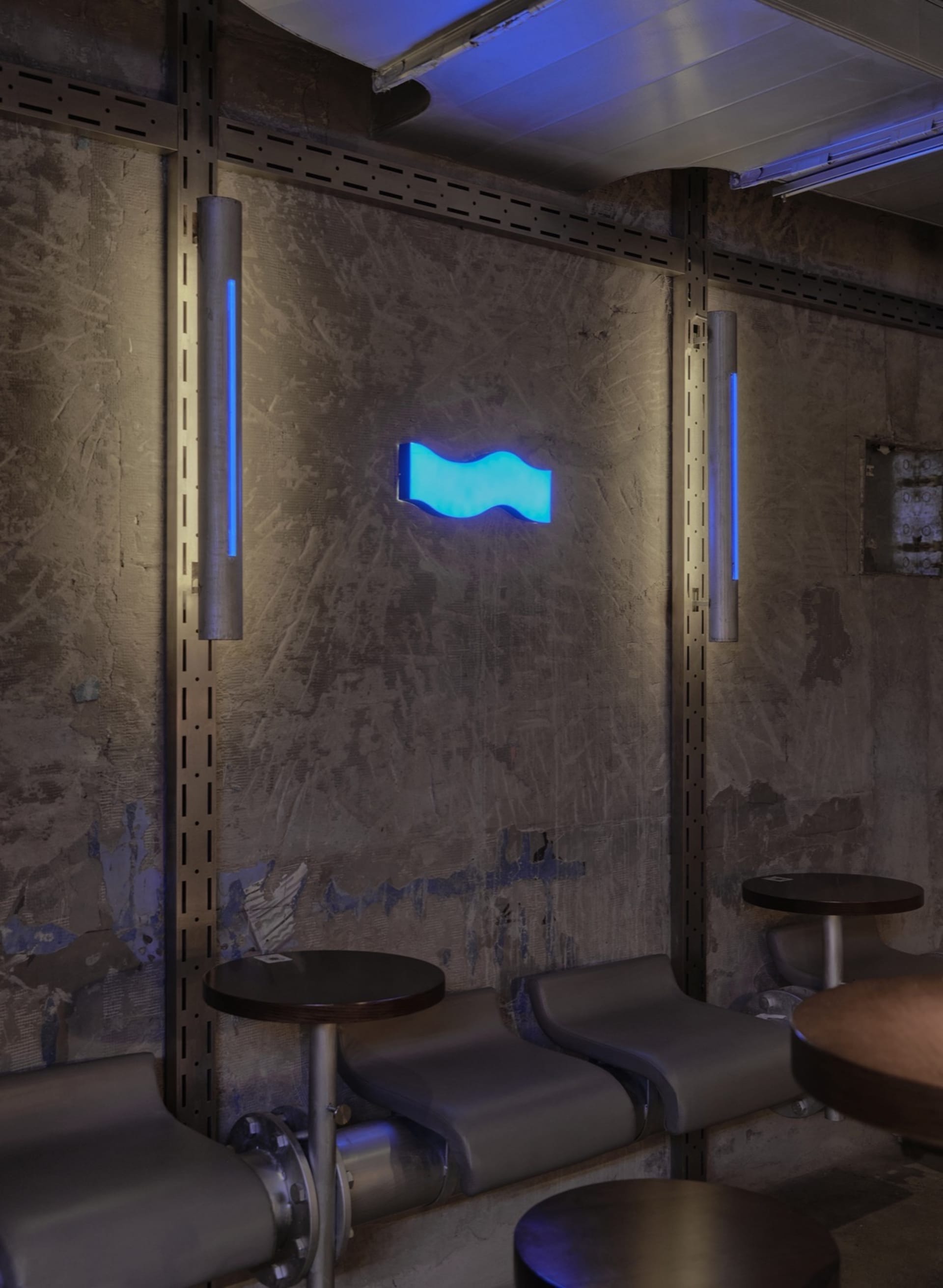 A modern cafe with blue-lit walls, dining tables, and chairs, set in a stylish and inviting atmosphere