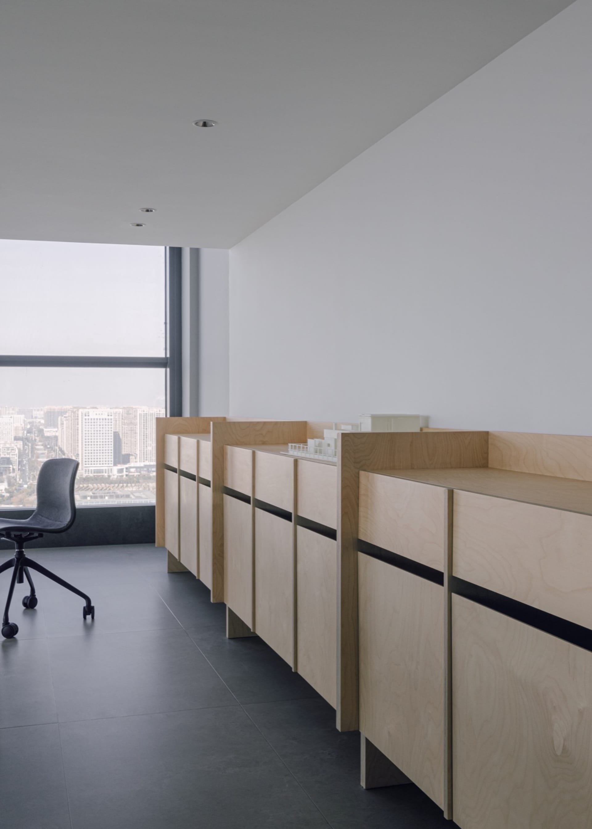 Office space with two desks, chairs, and cabinets, offering a view of the city outside through a large window