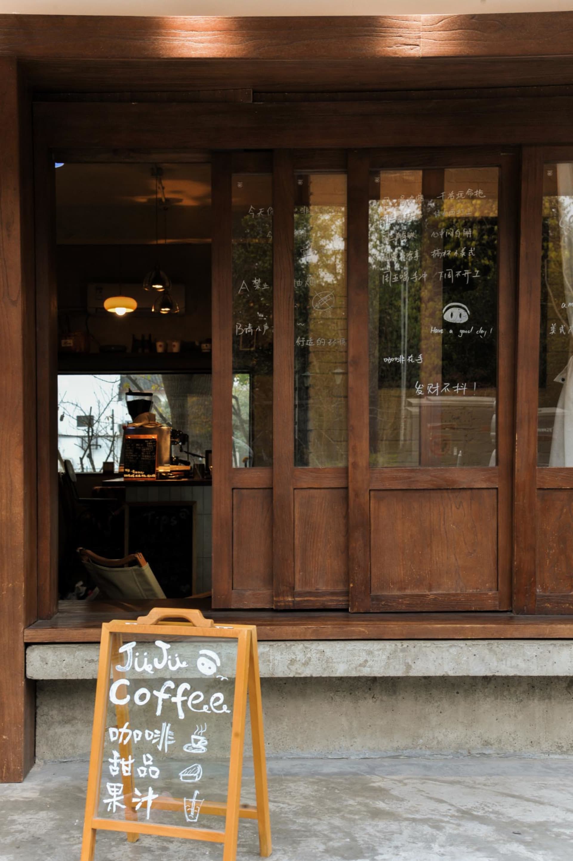 A cozy coffee shop with wooden walls, a window display, and comfortable seating areas, featuring a dining table and couch, with cups and bowls scattered throughout the scene