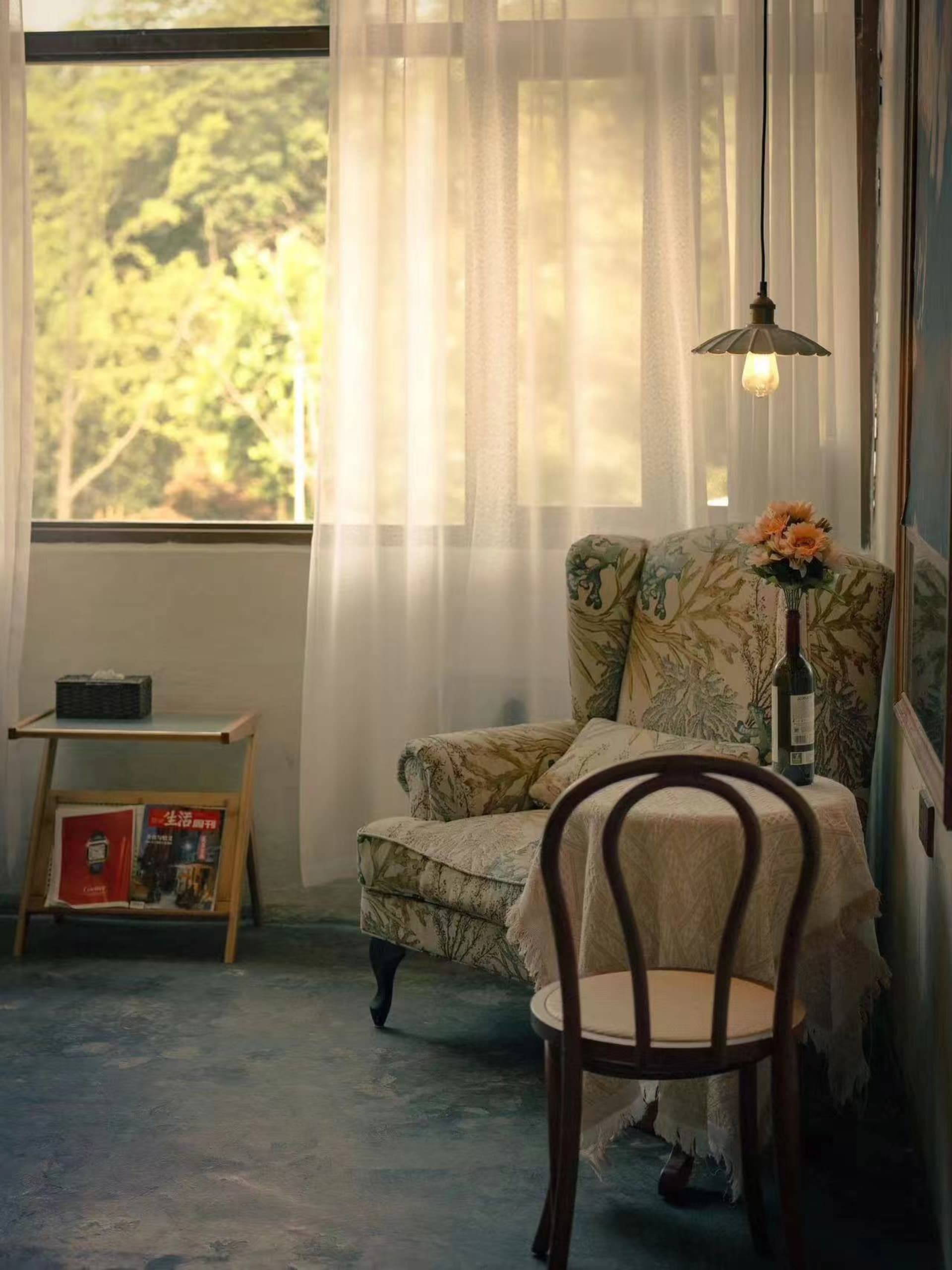 Cozy living space with a chair, cushion, and dining table, surrounded by books and a vase, in front of a window