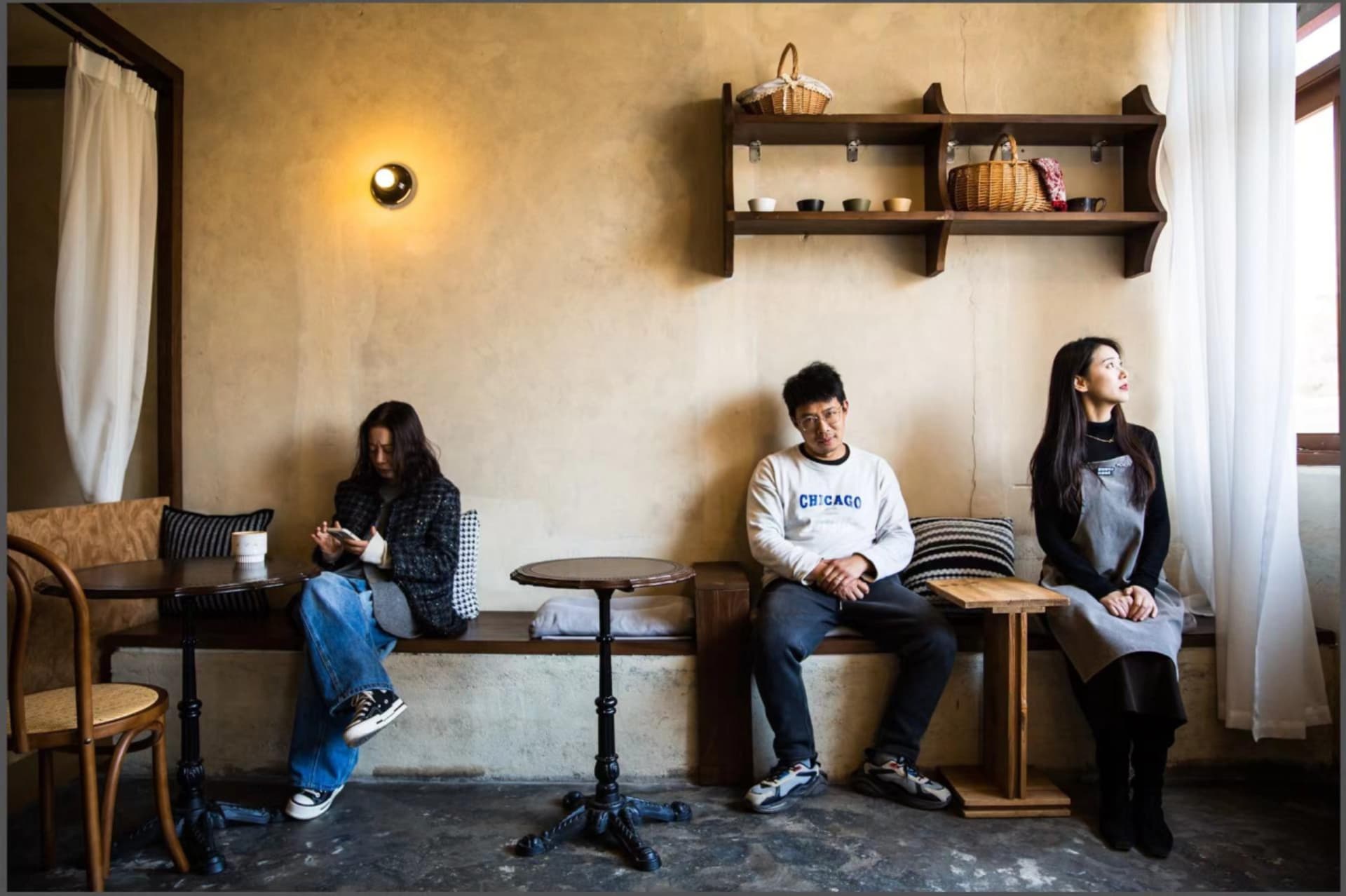 一群人在亞洲餐廳的木製長椅上就坐，周圍環繞著碗盤、杯子和手提包，營造出社交聚會或用餐的氛圍