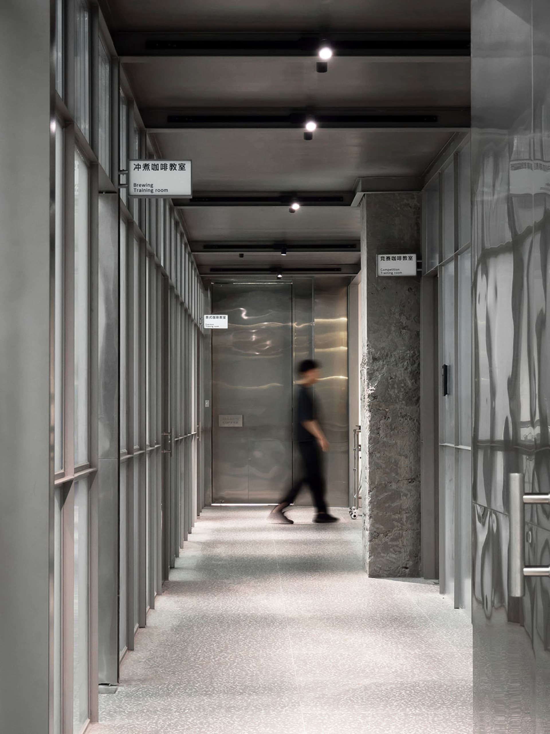 A modern hotel lobby with a silver metal finish, featuring two individuals walking down the hallway