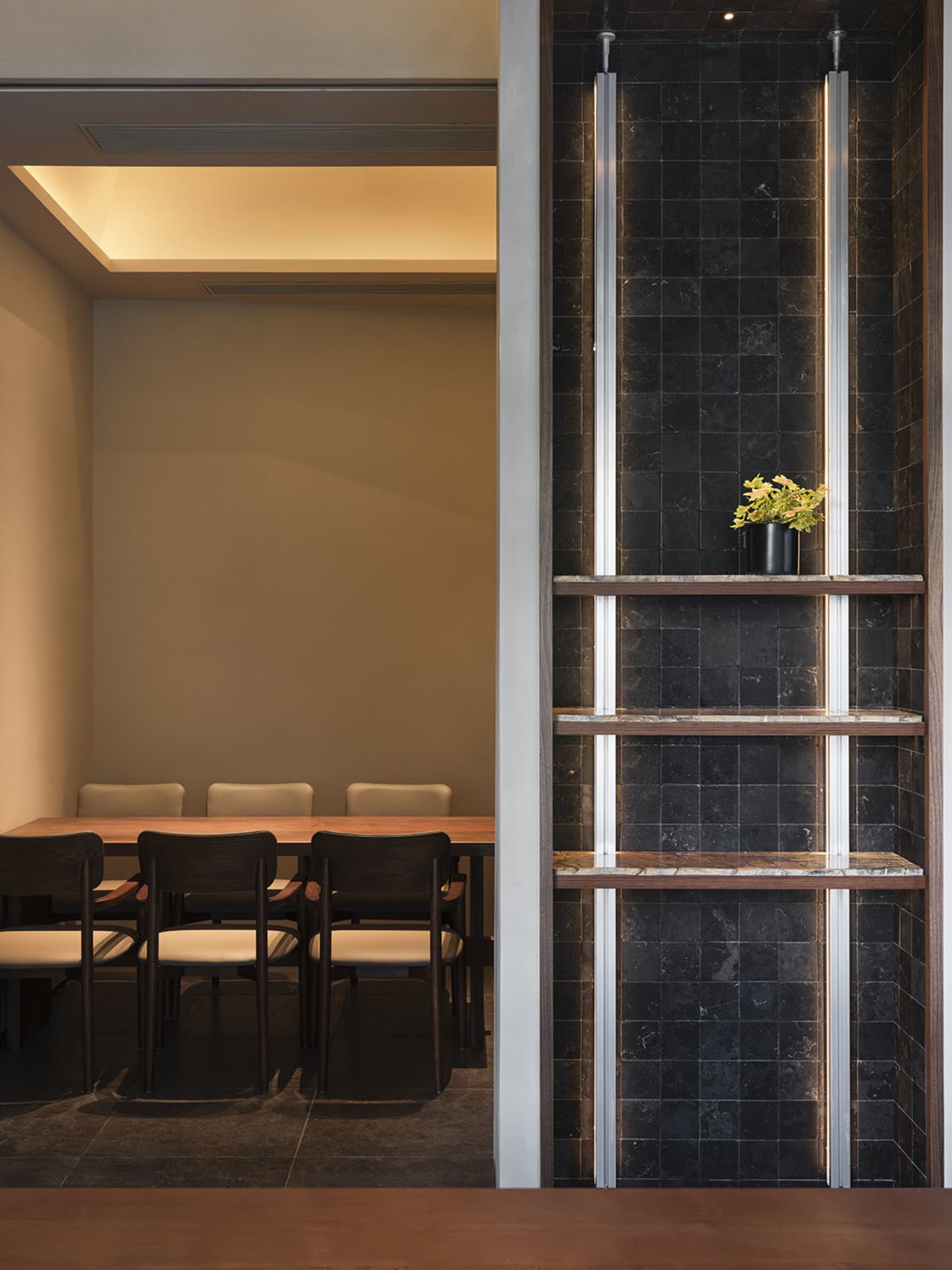 A well-lit dining area with a long table and multiple chairs, surrounded by modern architecture-inspired design