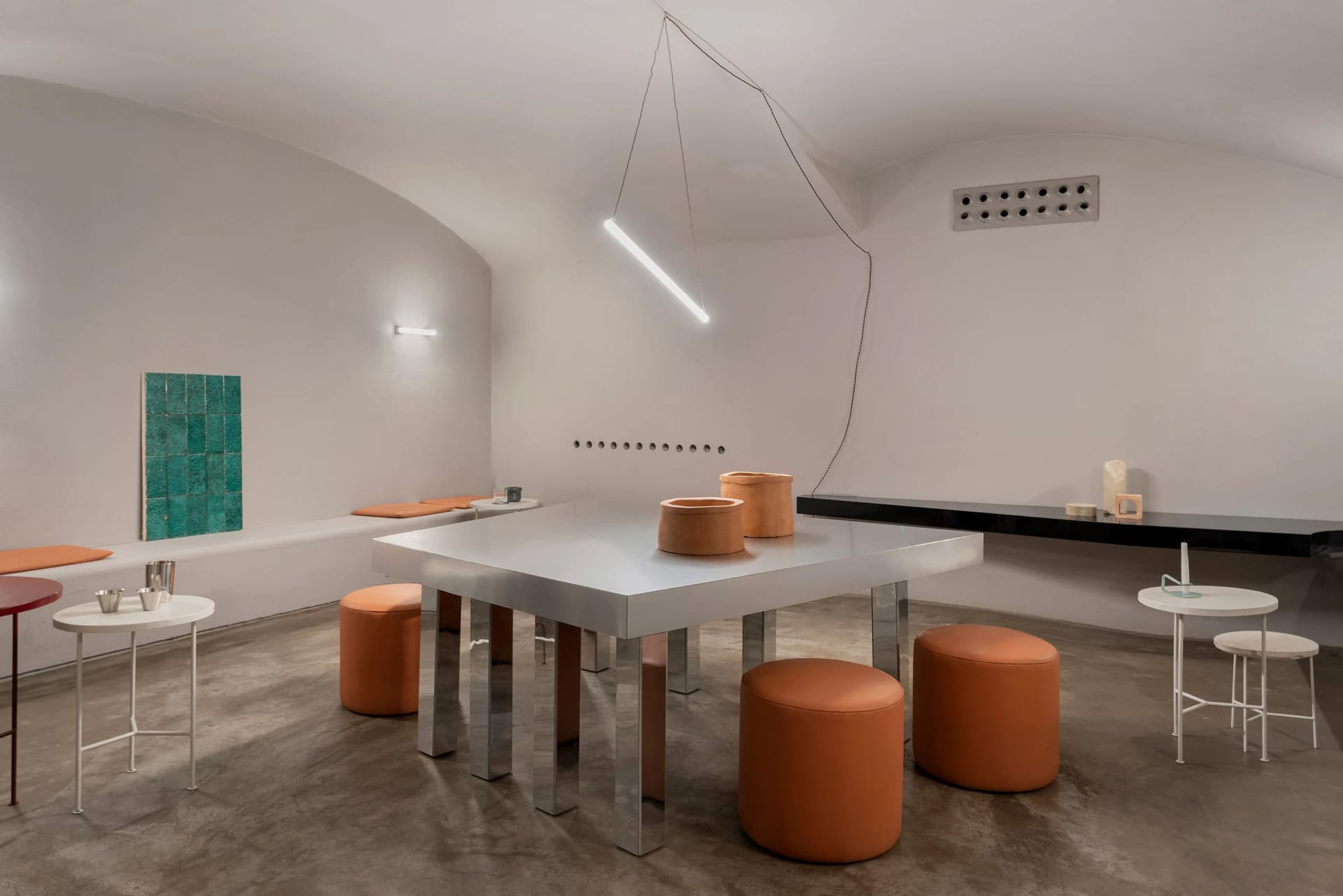 A modern cafe with a white table and orange stools, surrounded by chairs and natural light from windows