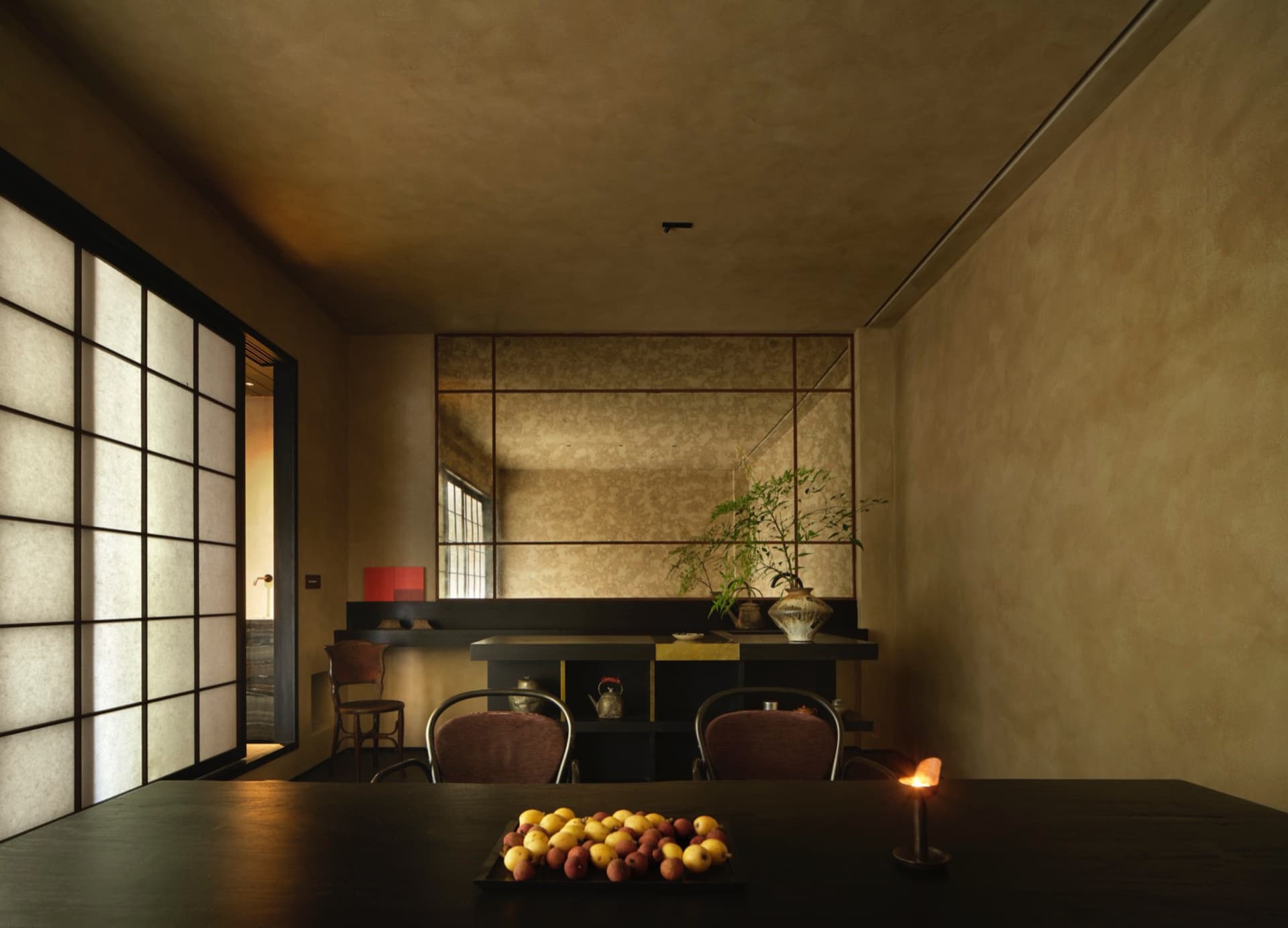 Cozy dining space with a concrete wall, a dining table, chairs, fruit, and cups