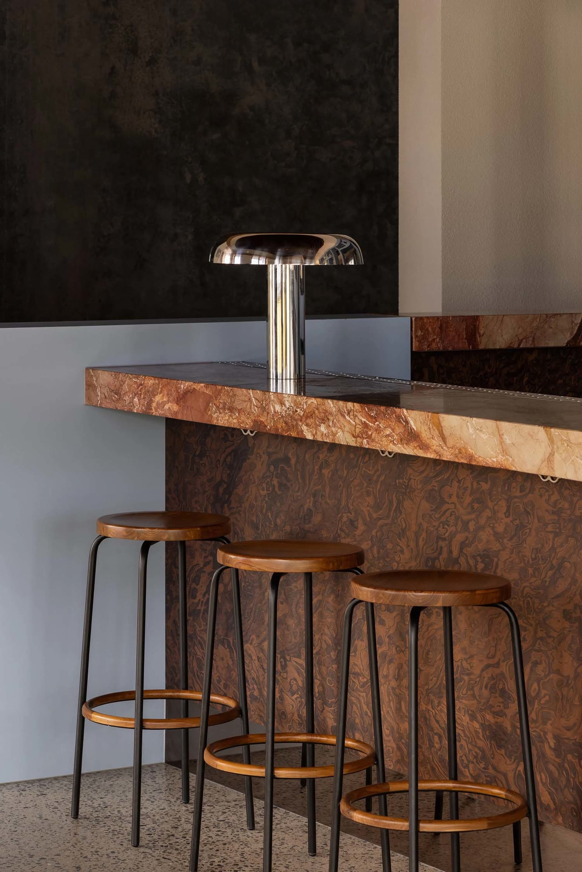 A modern bar with a marble countertop and wooden stools, inviting and comfortable atmosphere for socializing and enjoying drinks
