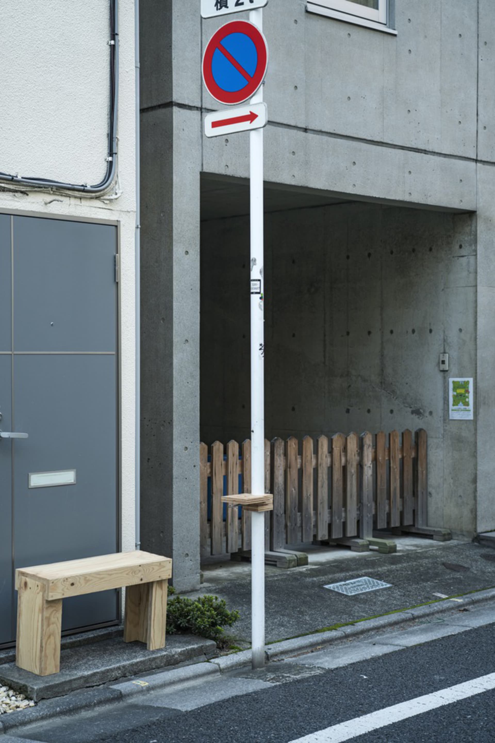 A street corner with a white pole and red sign, featuring benches and a mix of concrete and wood elements