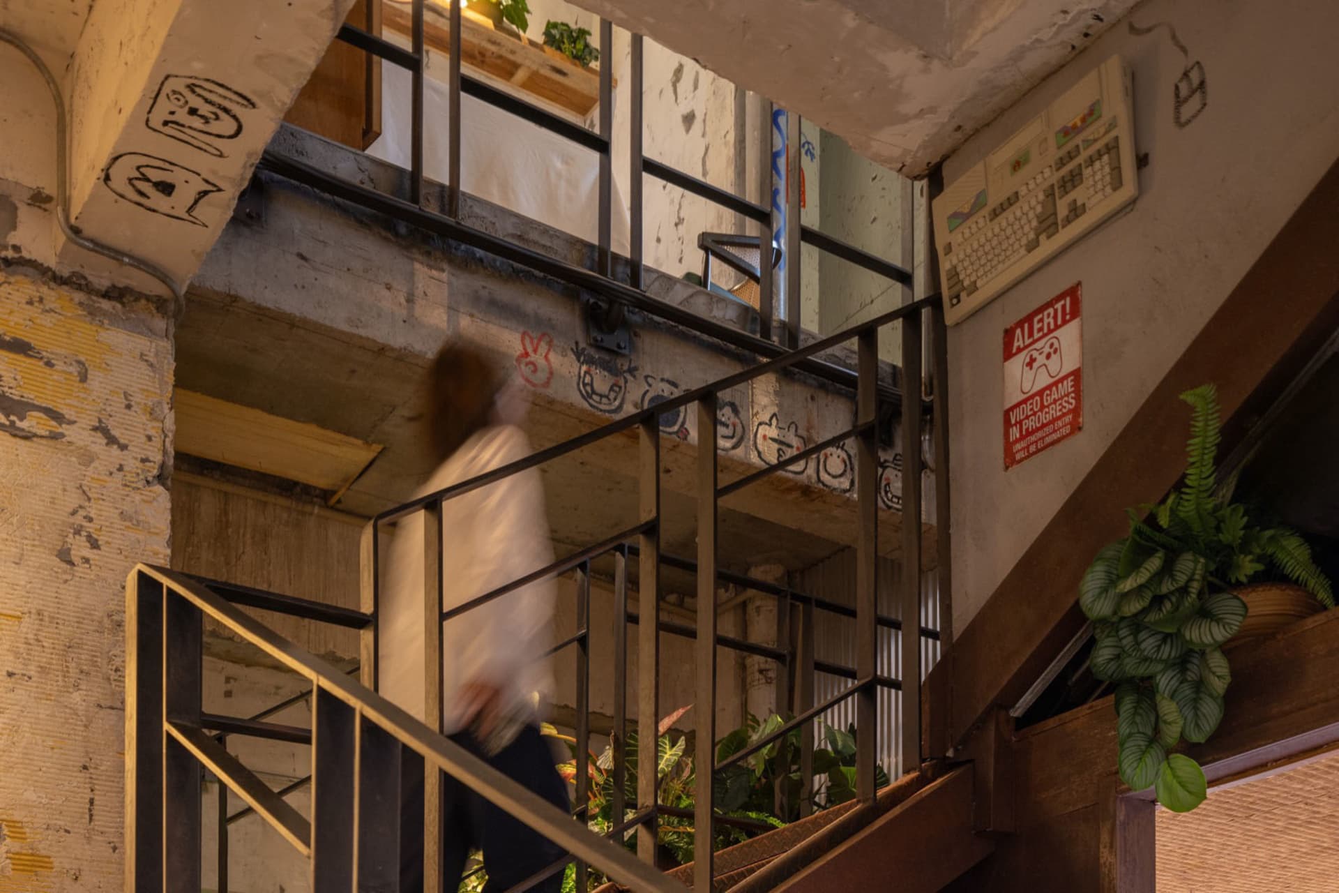 A woman walks down a concrete stairwell with two potted plants on the steps, suggesting a functional building with industrial features