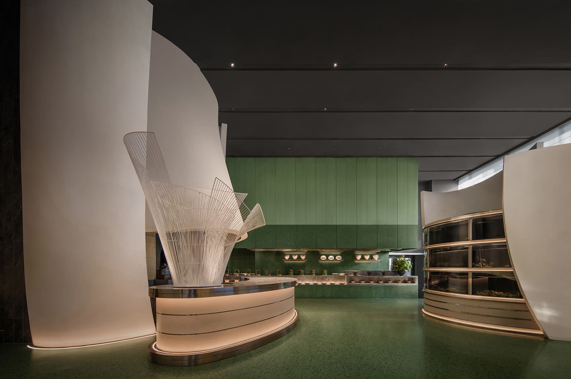 Modern restaurant interior with a large green wall, metal counter, and potted plant, featuring a welcoming atmosphere