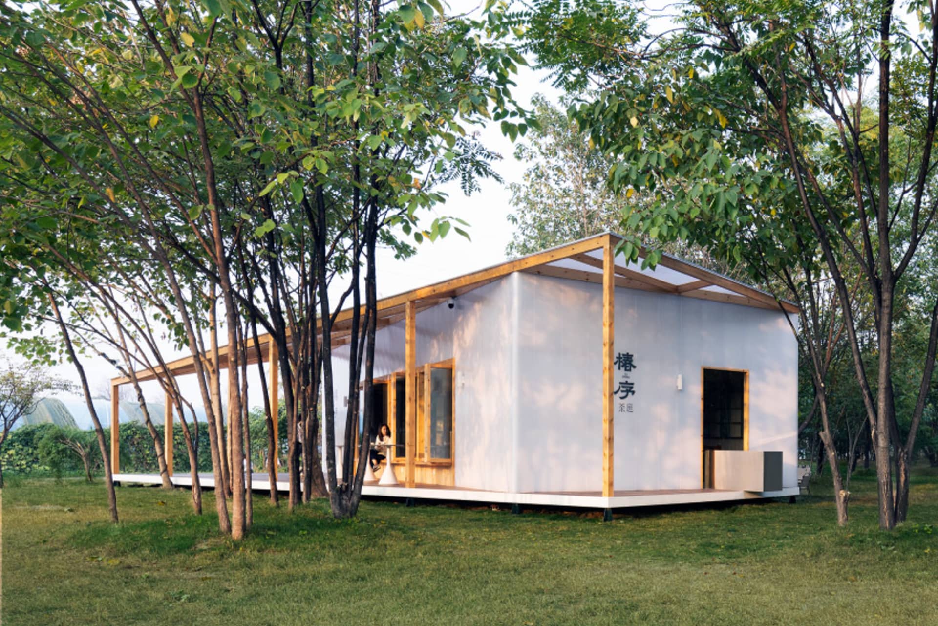 Asian-style house with a wooden structure, blending traditional and modern elements, situated in a serene natural setting with a grassy area and trees