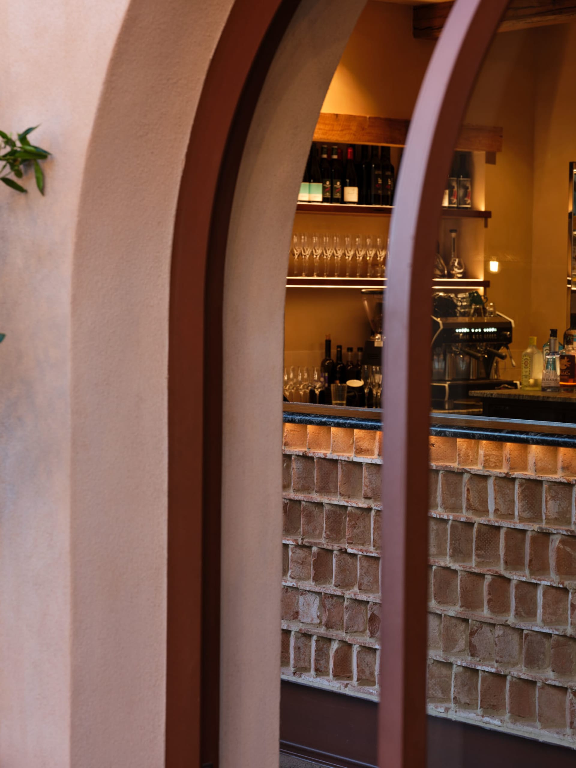 Cozy bar area with a brick wall, wooden countertop, wine glasses, and bottles, inviting atmosphere for socializing