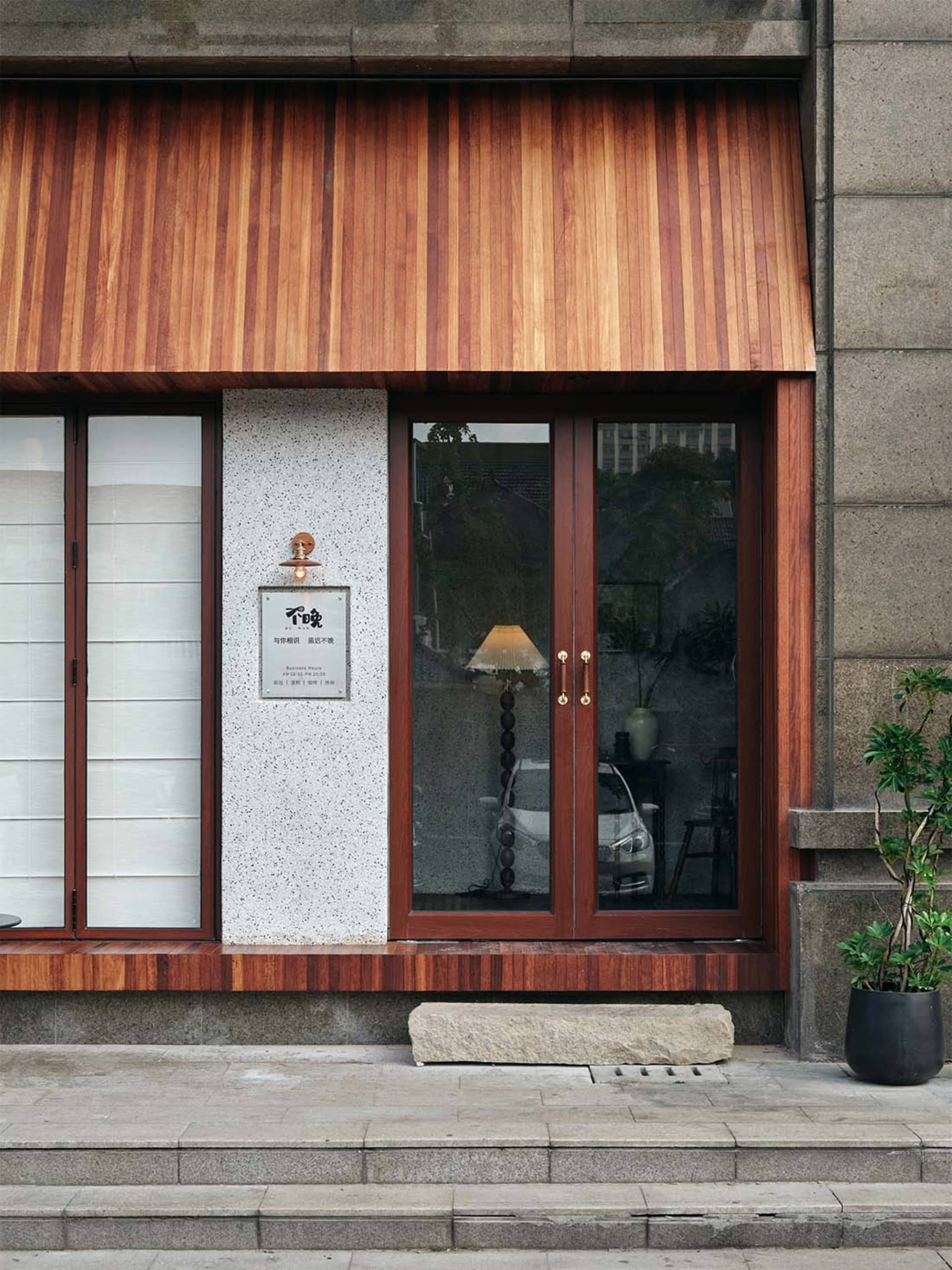 Exterior building facade with a wooden doorway, stone base, and large window allowing natural light to enter