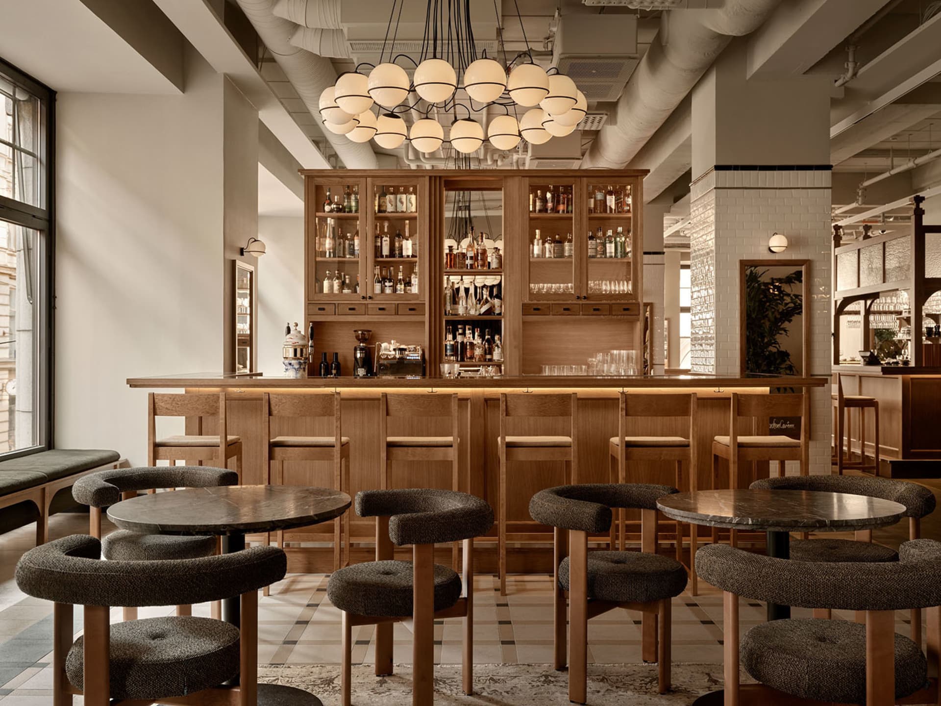 A cozy bar area with wooden tables and chairs, featuring bottles and a warm atmosphere for socializing and enjoying drinks