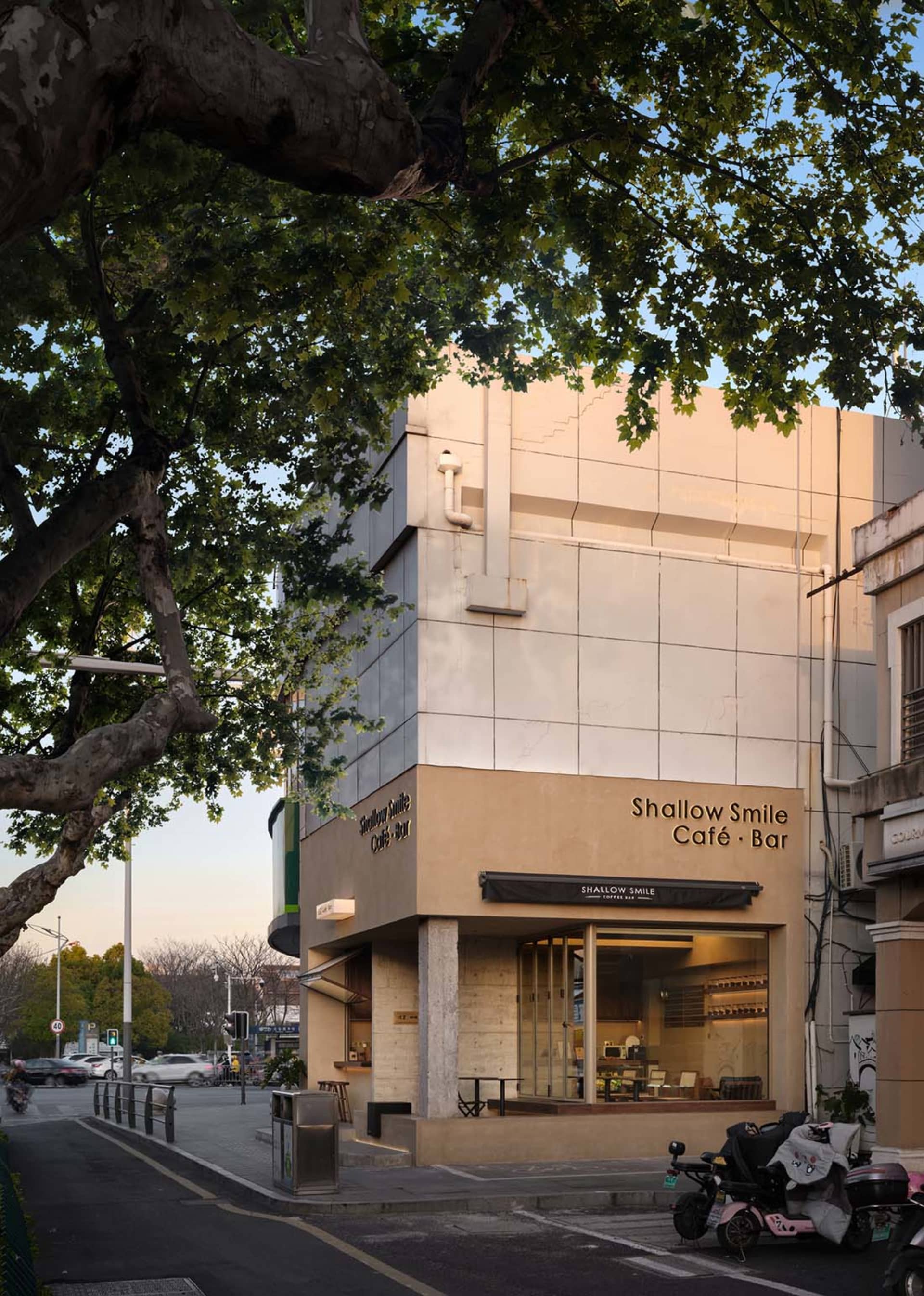 A modern cafe with a white concrete facade, large windows, and a urban atmosphere, surrounded by parked cars