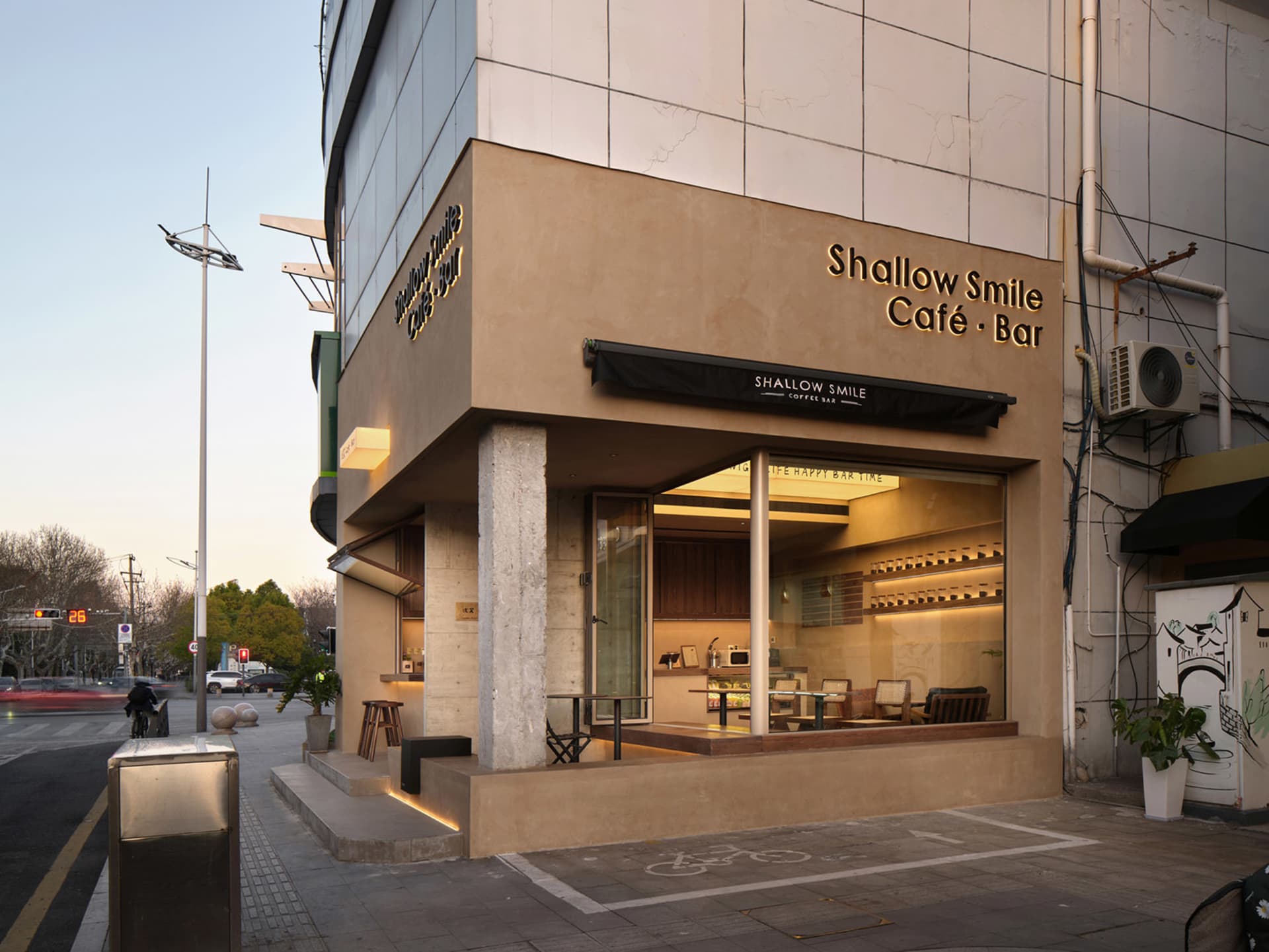 A warm and inviting cafe with a large window, seating areas, potted plants, and natural light