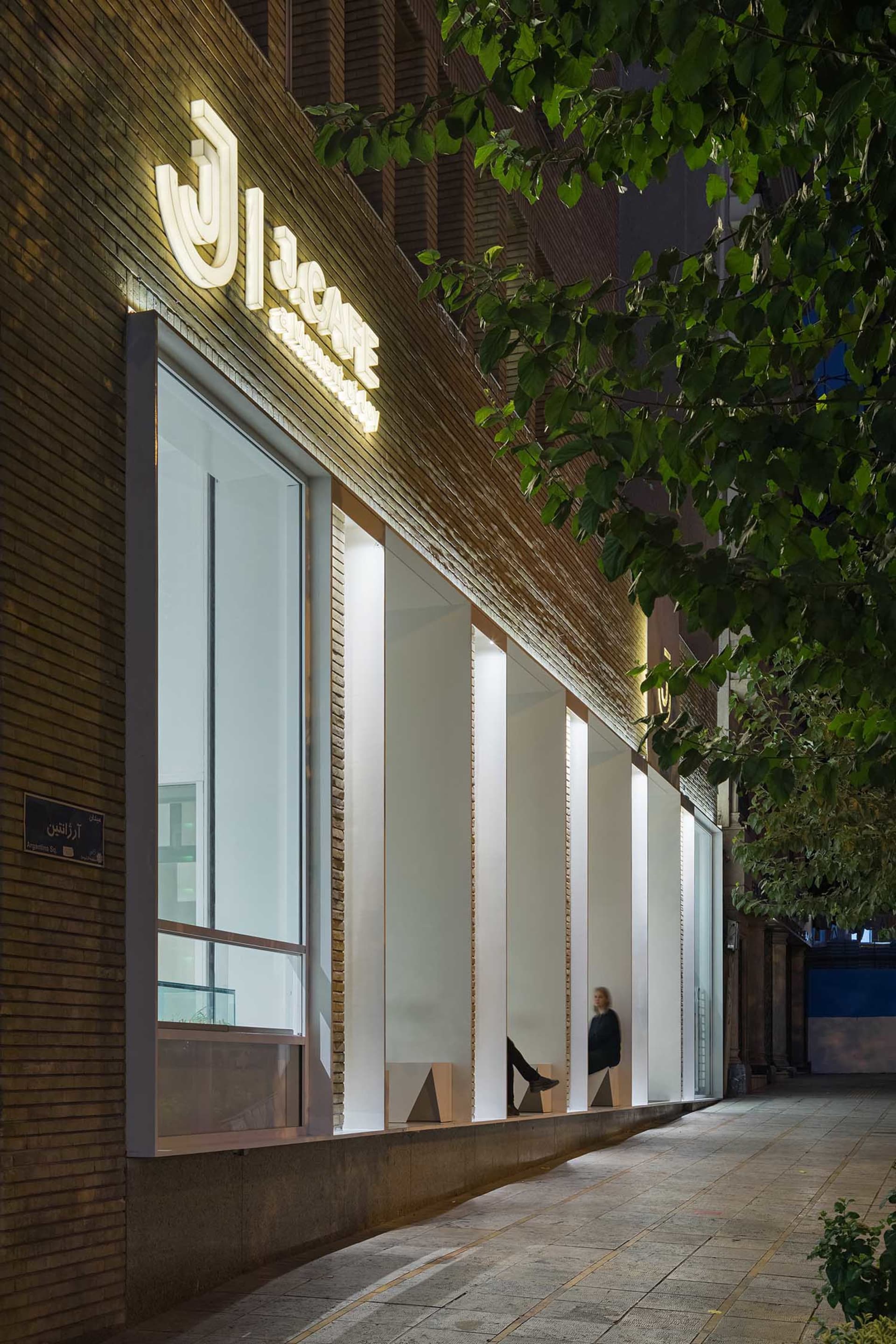 A classic storefront at night with a brick facade, featuring three people sitting on benches outside, enjoying the calm atmosphere