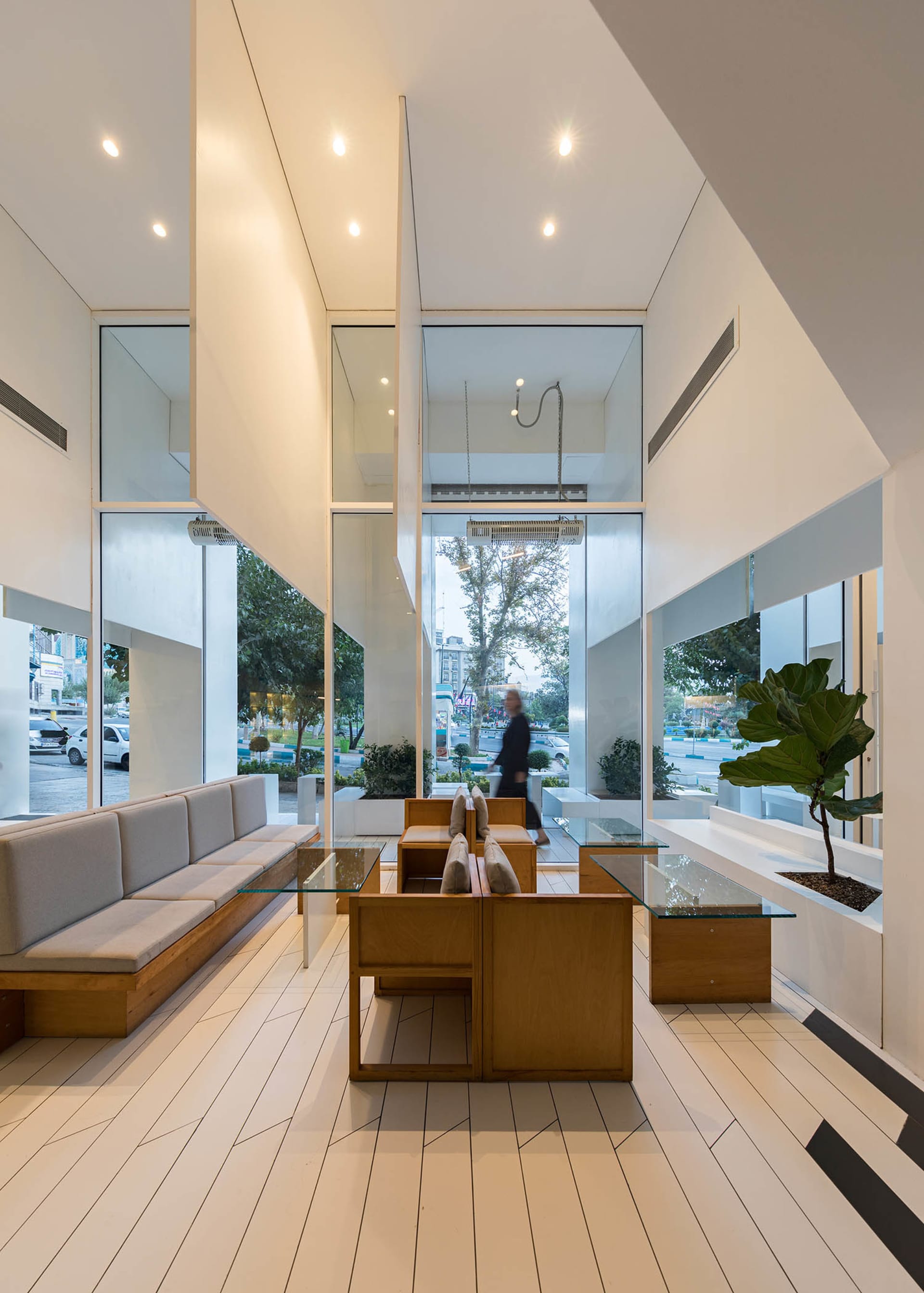 A modern public space with glass walls, natural light, and various seating options, including couches, benches, and chairs, with potted plants adding to the lively ambiance