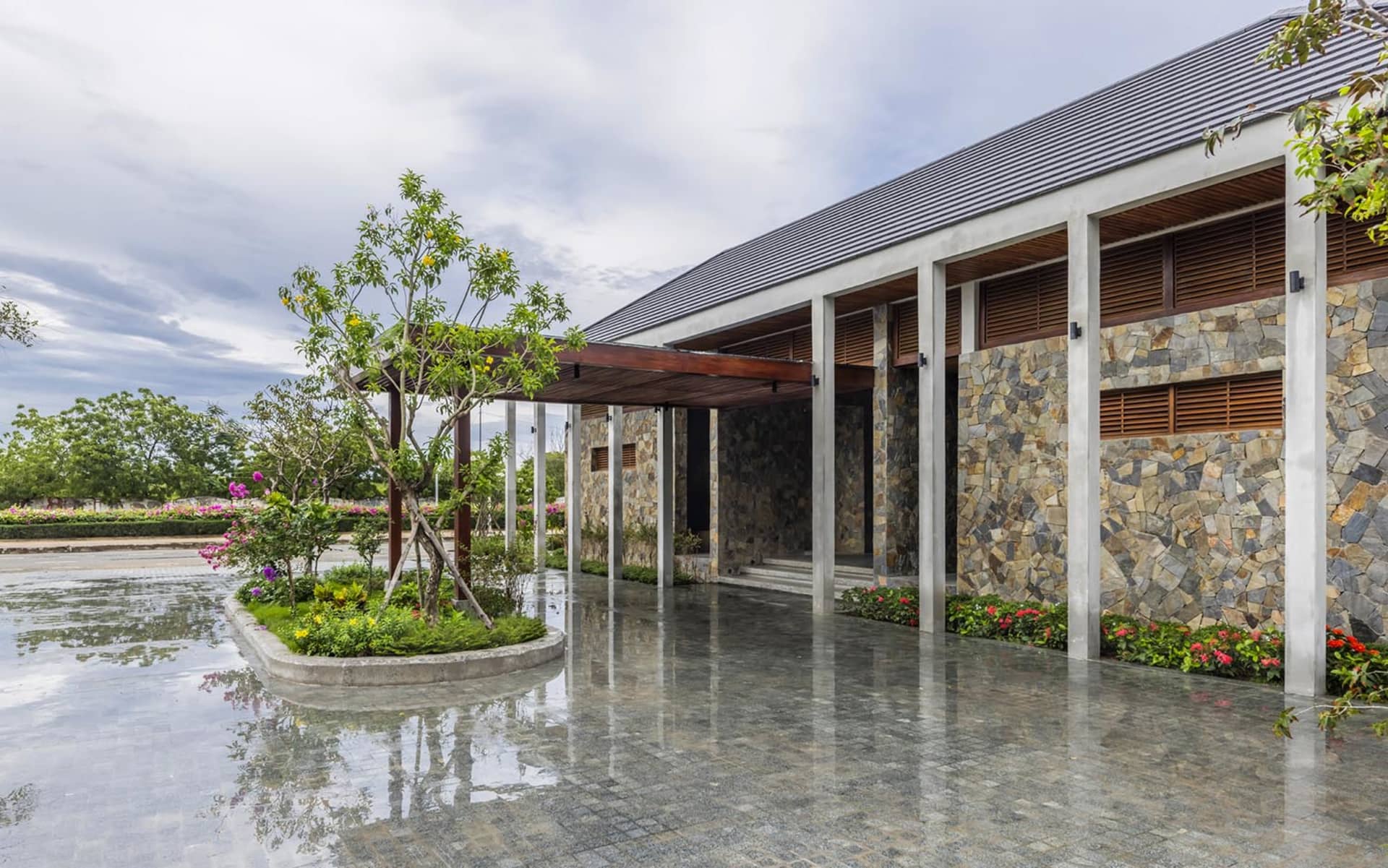 A modern house with a gray roof and wooden door, surrounded by a stone wall and potted plants, creating a serene and inviting atmosphere