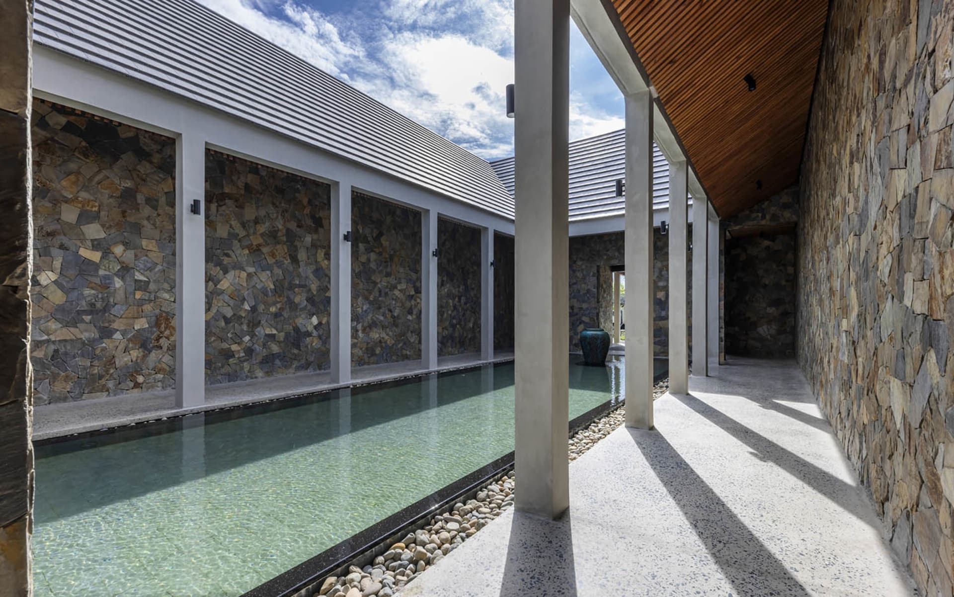 An indoor pool area with stone walls, empty pool, and lounge chairs in a luxurious and sophisticated environment