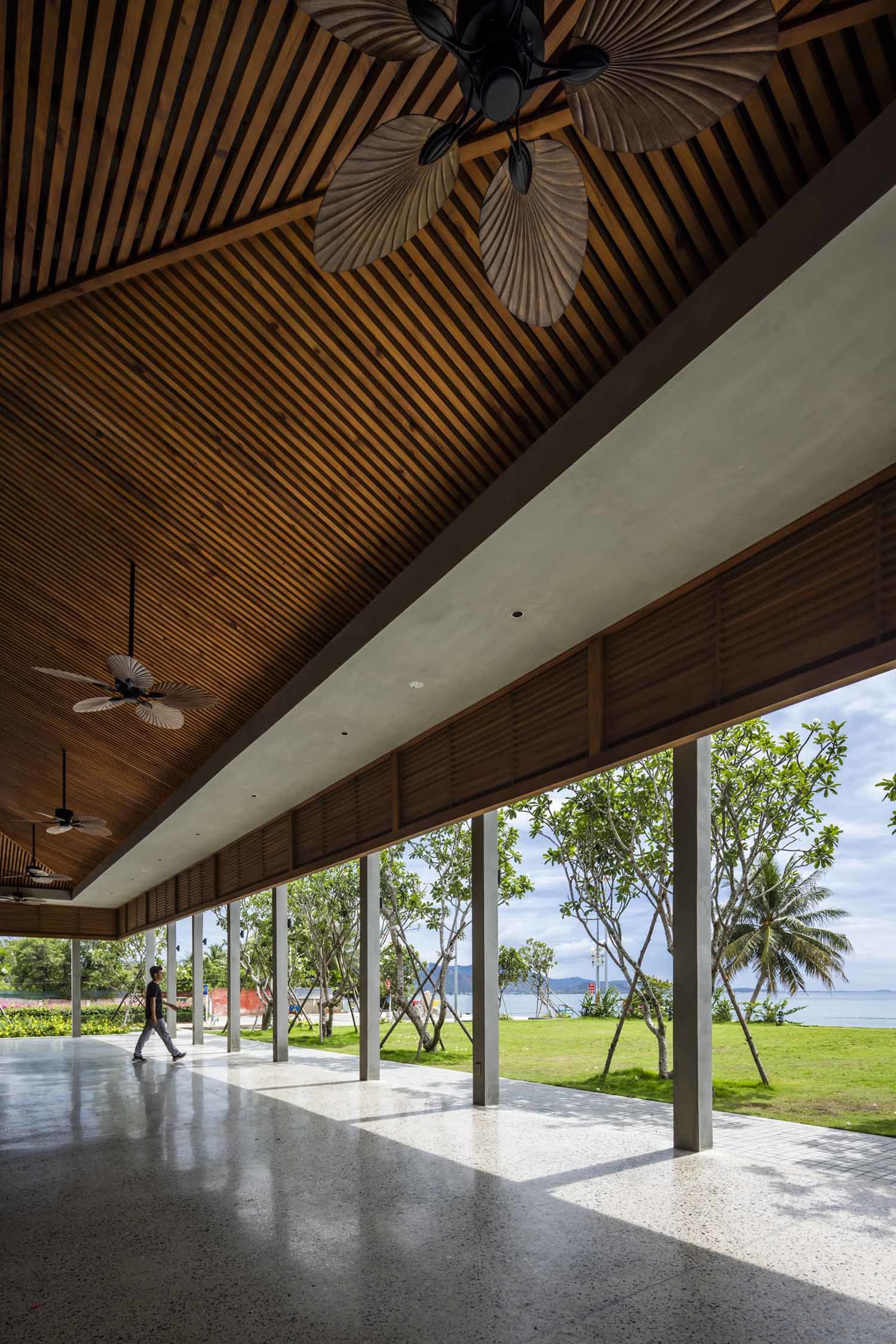Warm and inviting open-plan space with wooden beams, a large window, and natural light, featuring a living area and dining space with chairs and a person walking through
