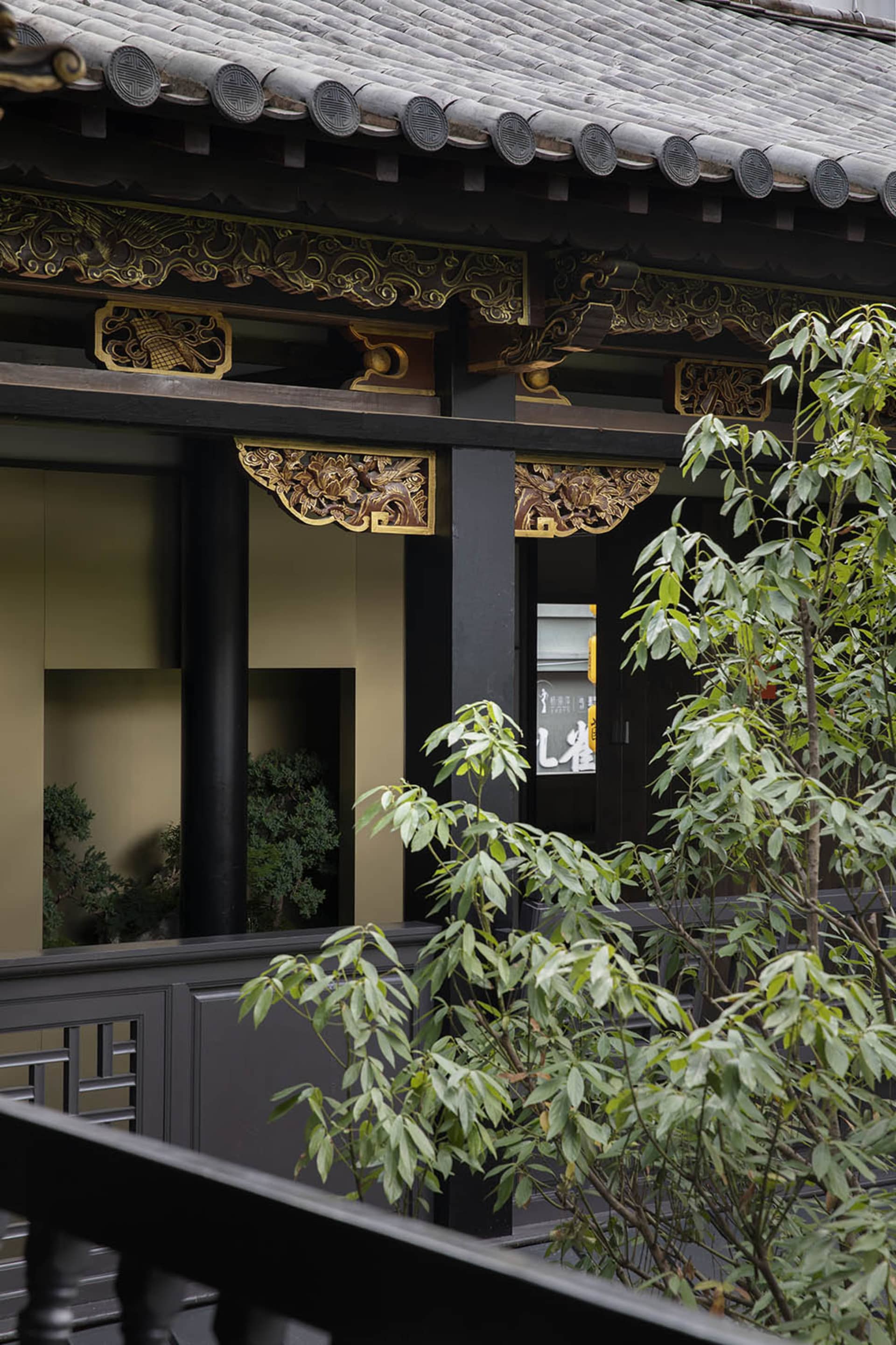 An Asian-style building with a balcony overlooking a garden area, featuring black pillars and gold accents, with potted plants adding to the serene ambiance