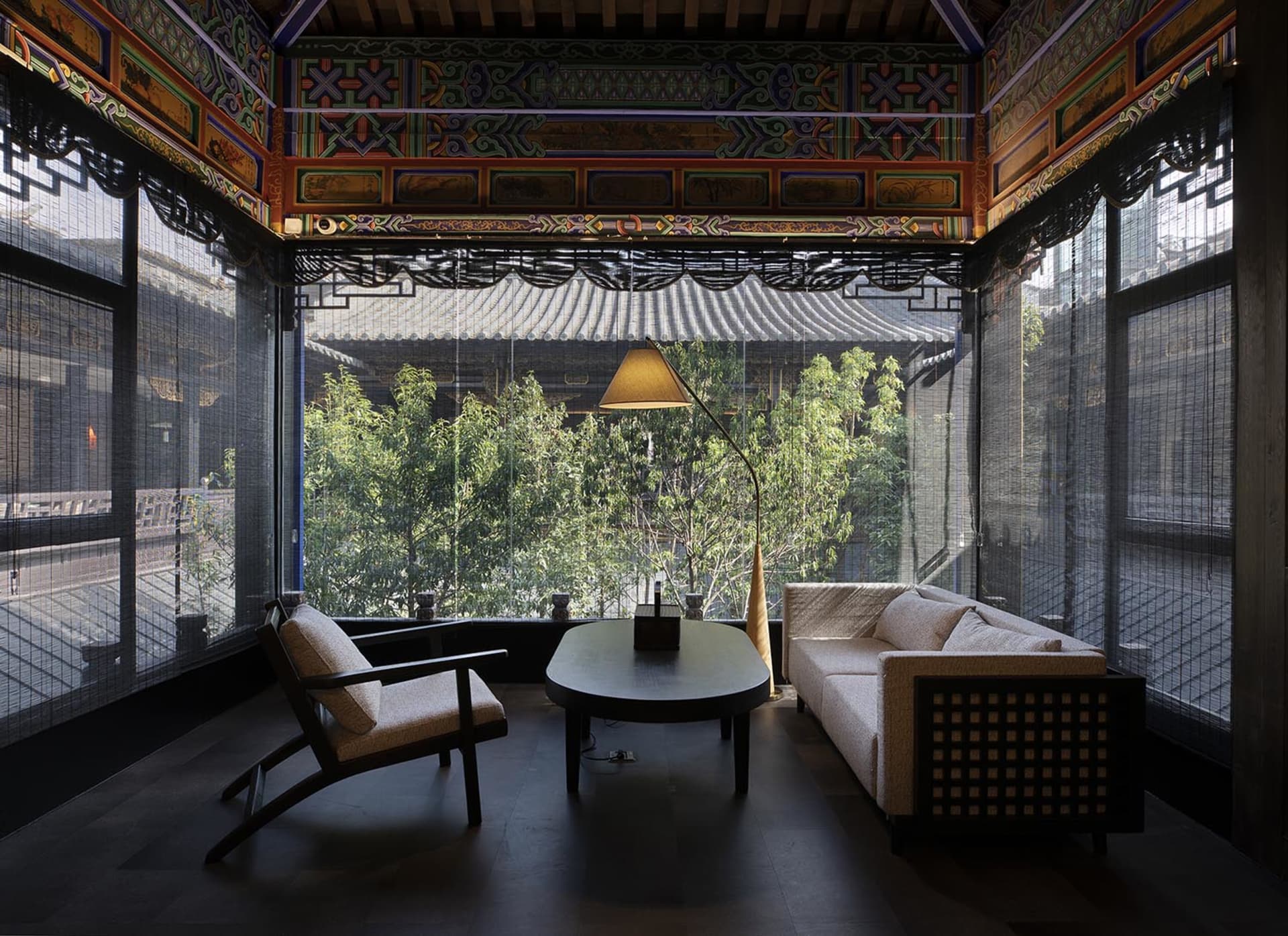 Asian-style living room with a large window, two couches, a chair, a dining table, and a potted plant, creating a warm and inviting atmosphere with a focus on comfort and relaxation