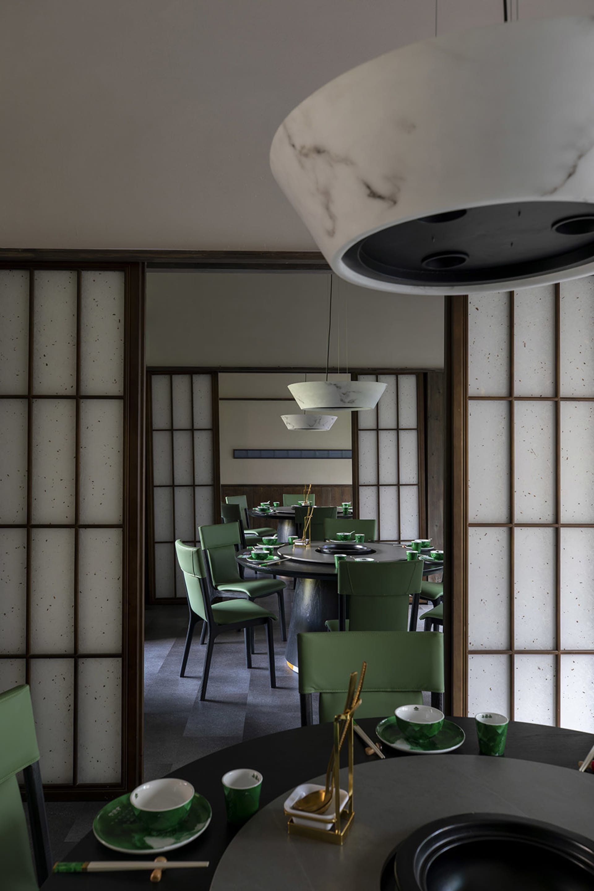 A modern restaurant interior with Asian-inspired decorations, dark wood flooring, and dim lighting, featuring tables, chairs, and tableware