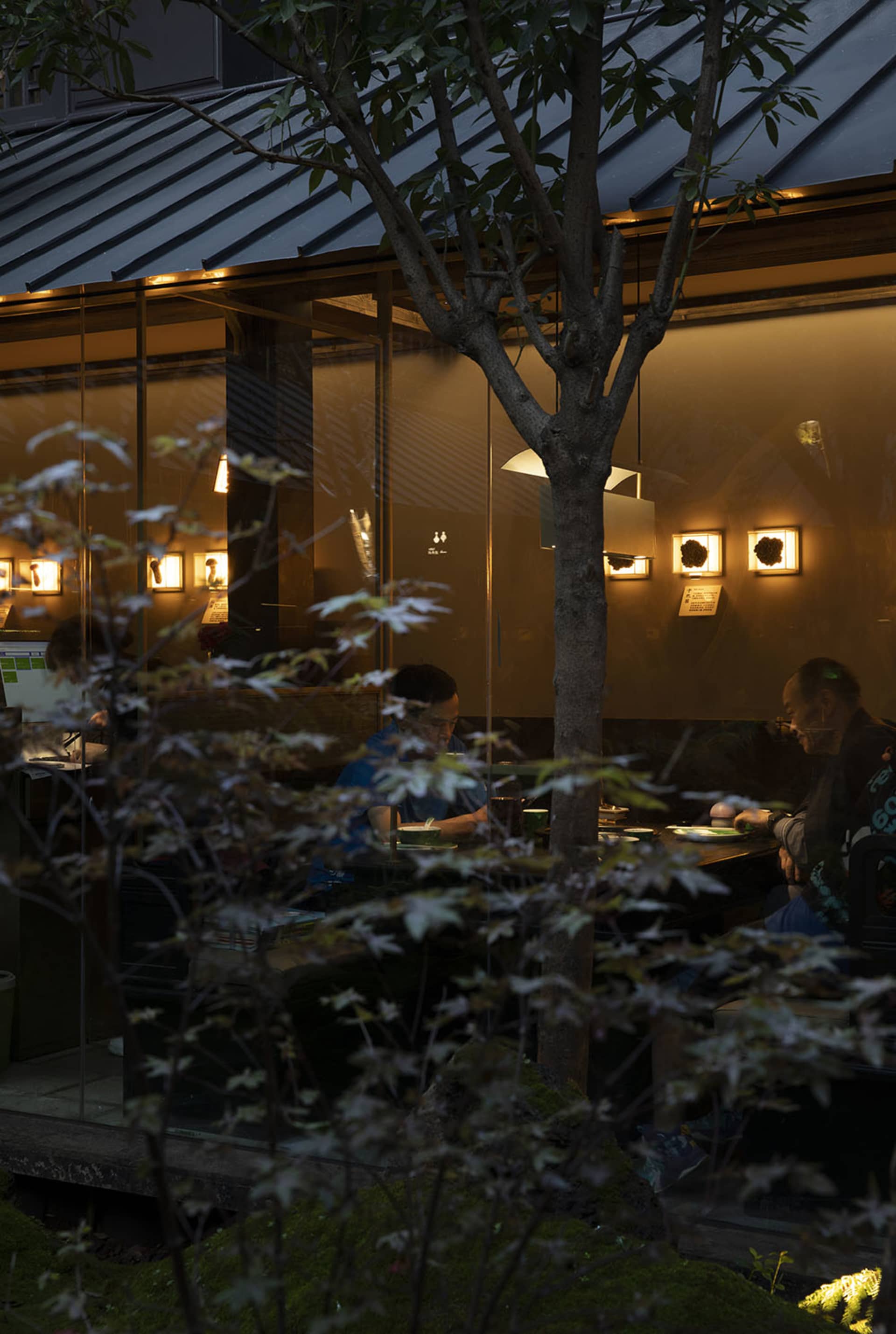 休閒餐廳區域，有人們在桌邊用餐，周圍環繞座椅，牆上掛滿藝術品，並融合自然光與人工照明