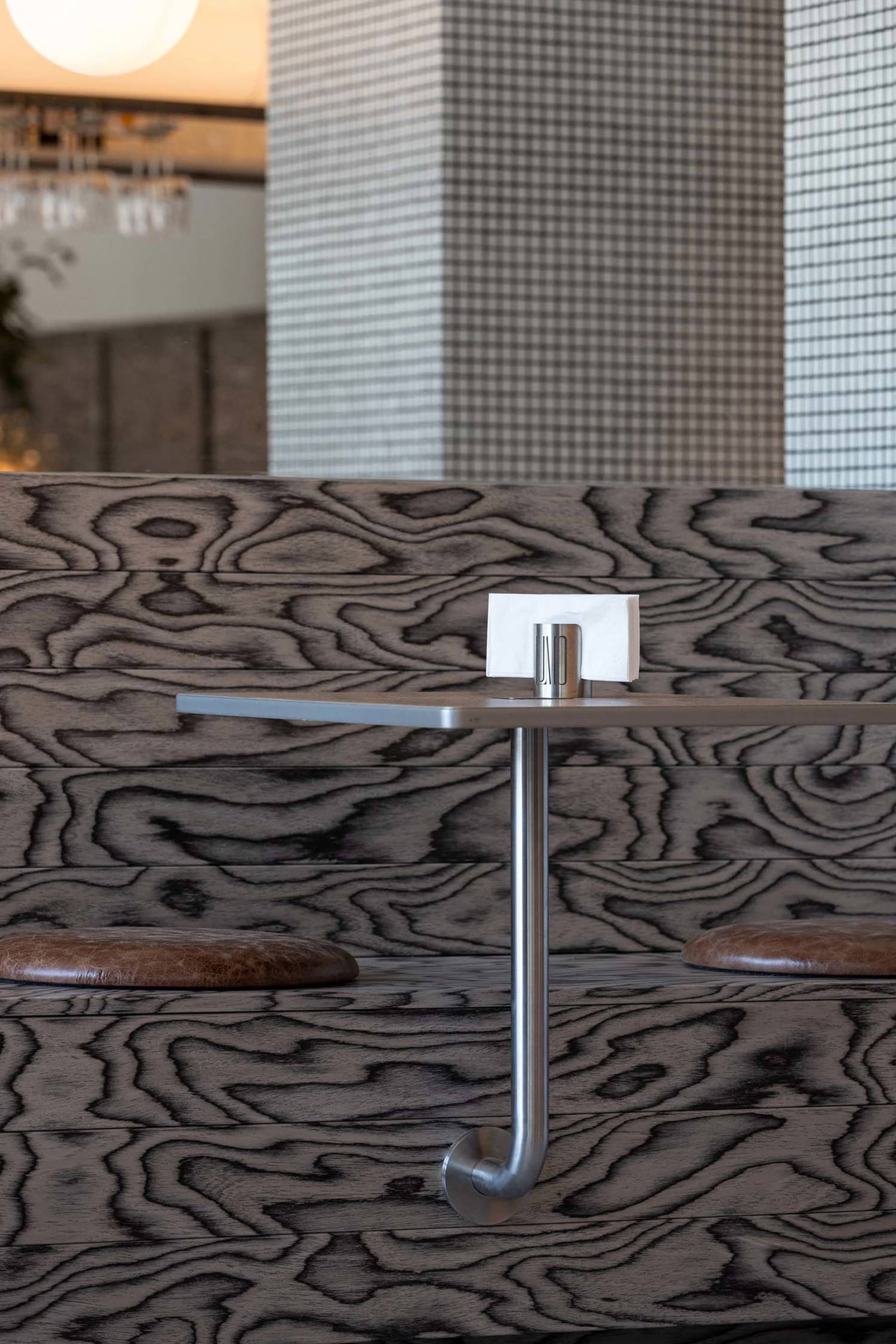 Dining table with silver base on a hardwood floor, surrounded by two chairs in a modern restaurant setting