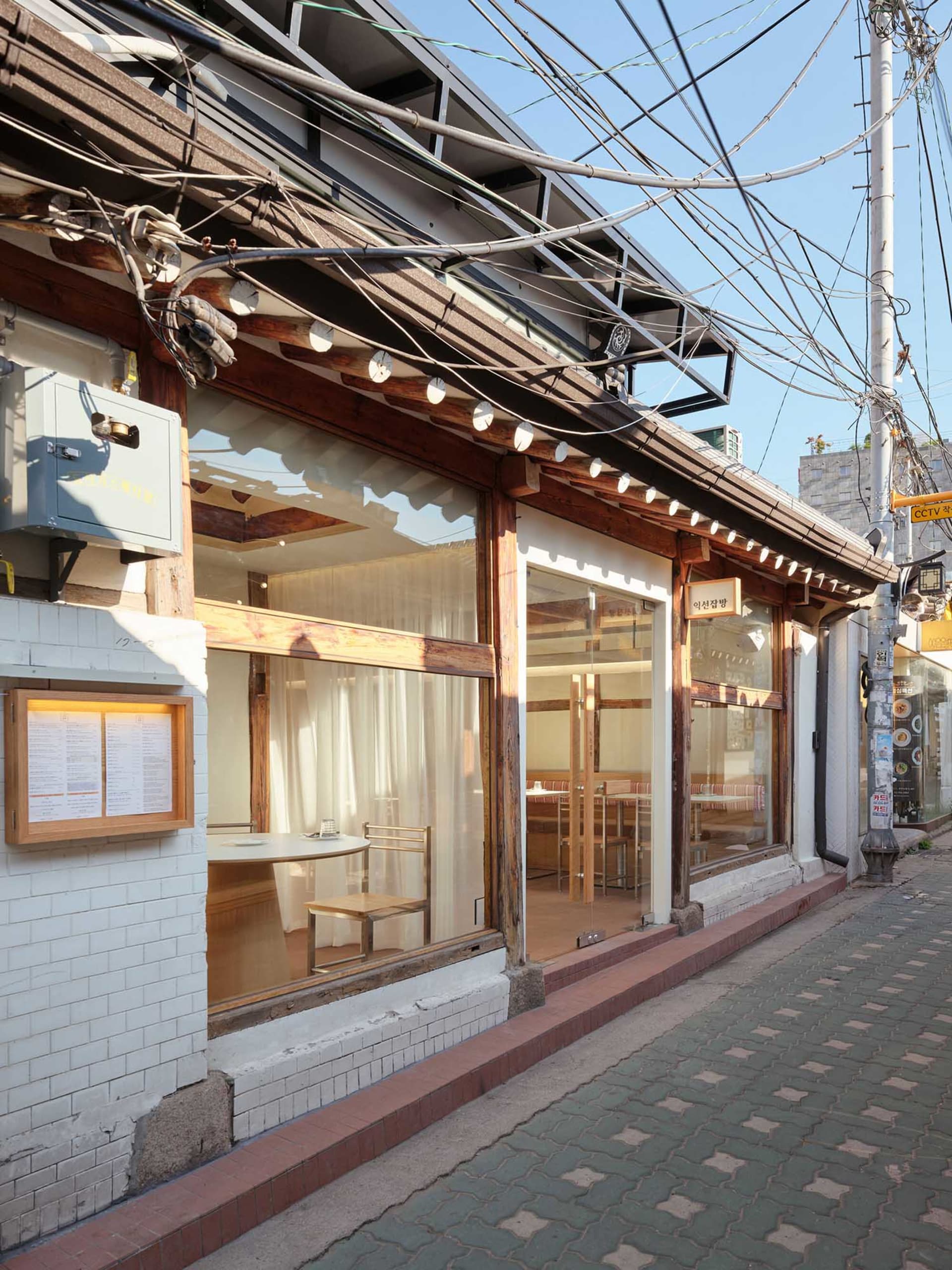 光線充足的木質內裝餐廳用餐區，設有多張桌椅、窗戶自然光線，以及白色桌巾