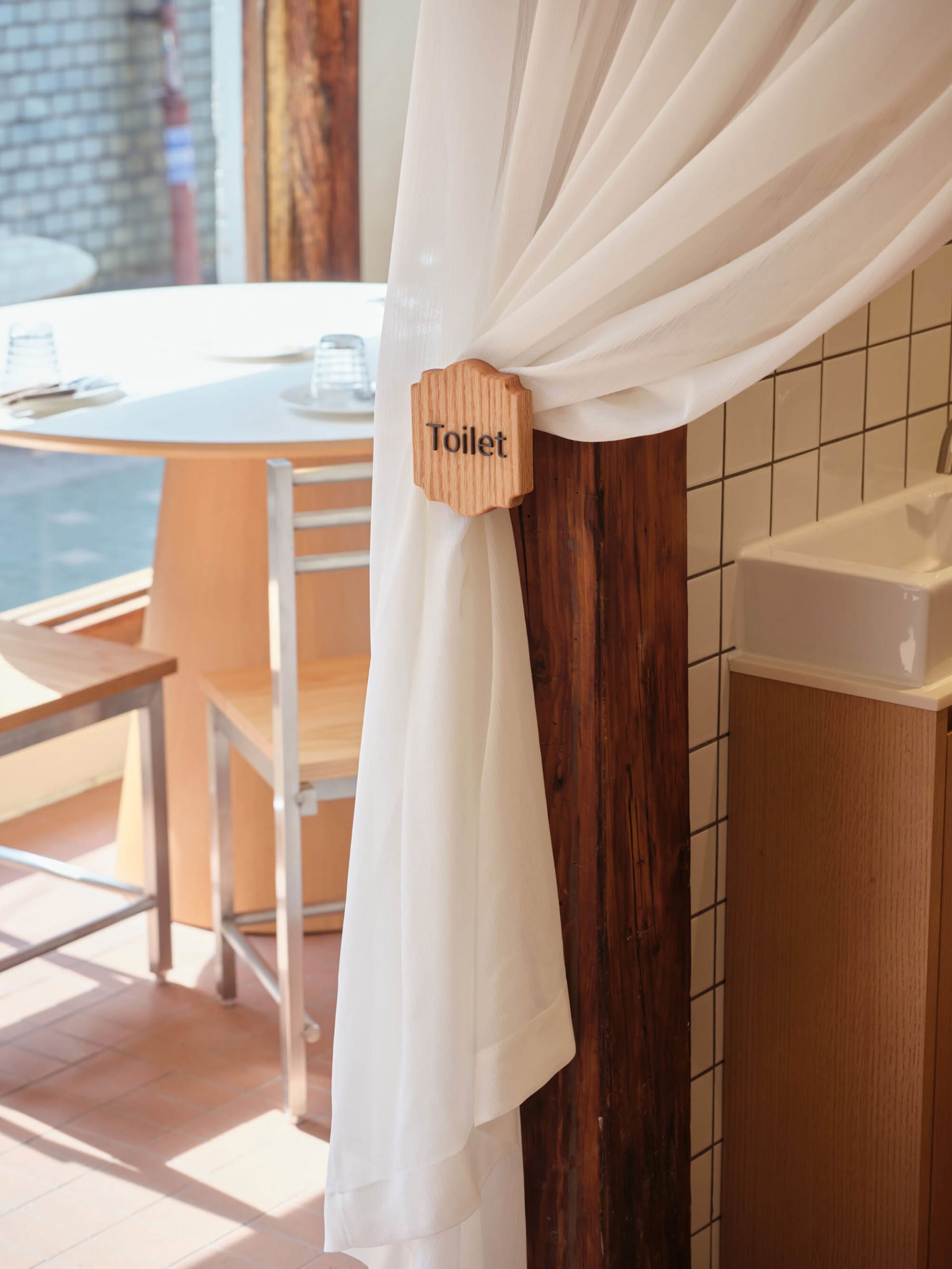 A clean and organized bathroom with a wooden door, white curtain, two chairs, and three cups, featuring a cozy atmosphere
