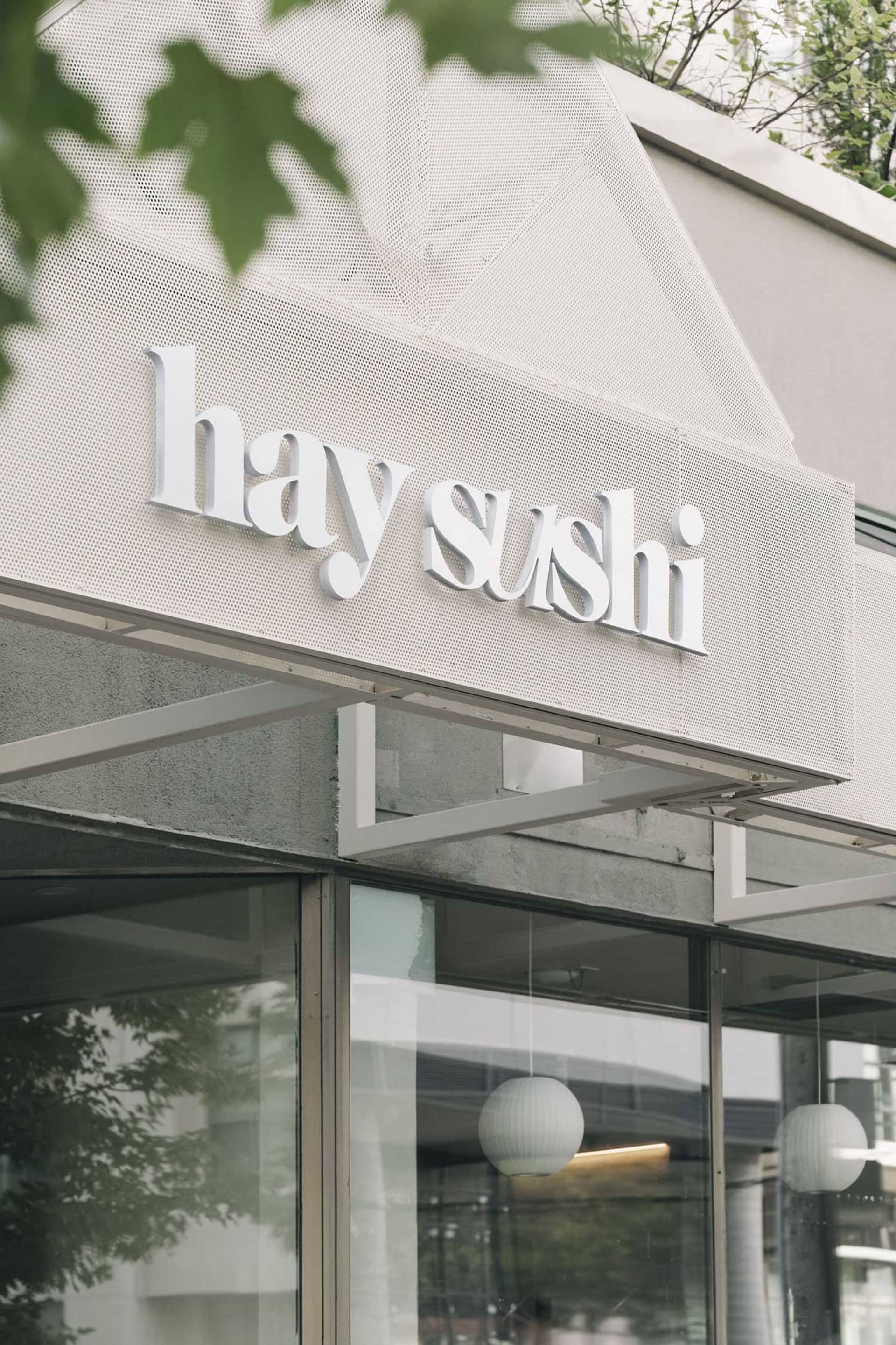 Exterior view of a modern sushi restaurant with a white facade and a glass front, allowing natural light to enter