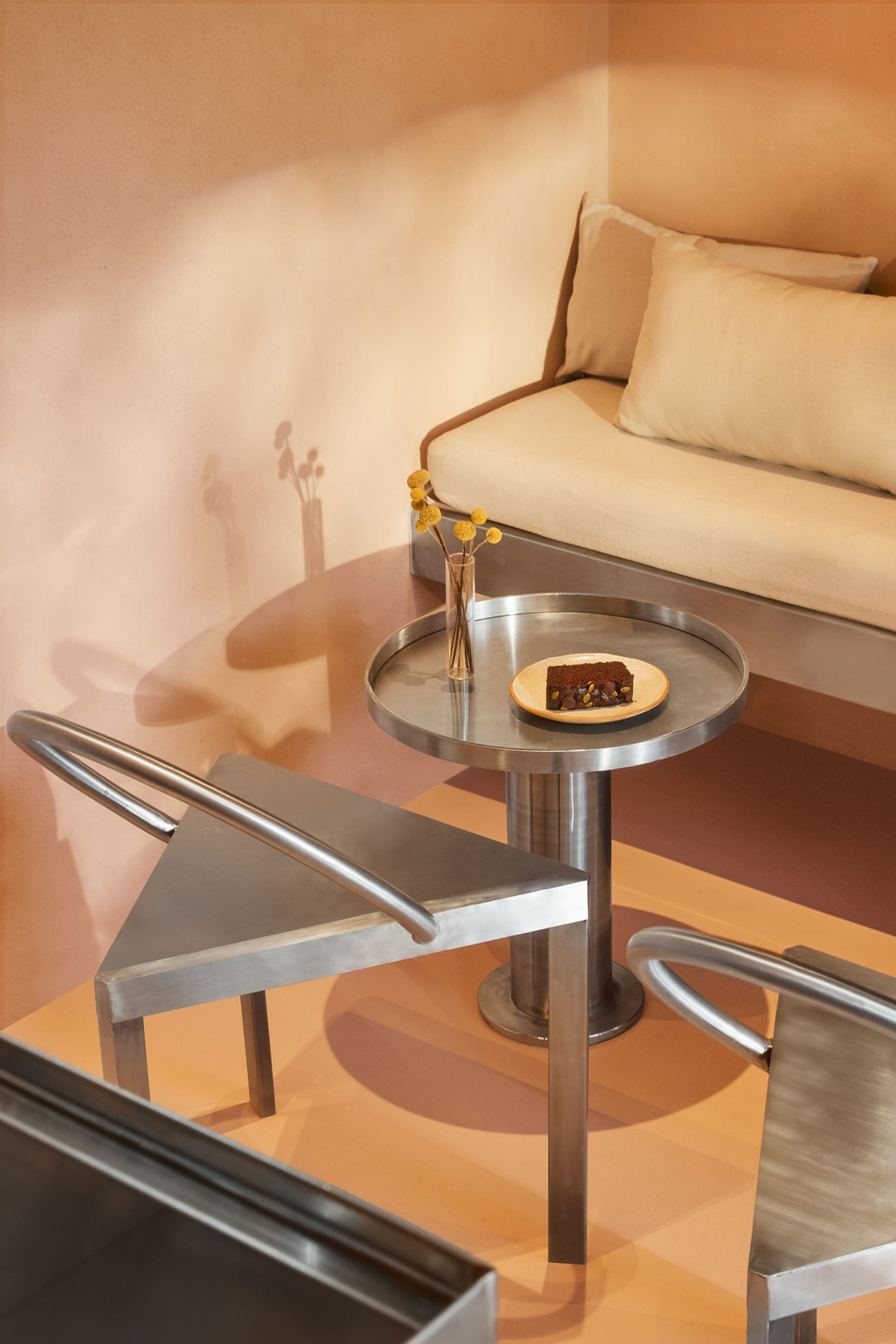 Cozy living space with a couch, chair, dining table, and small round table with a plate, surrounded by vases and featuring wood and metal materials