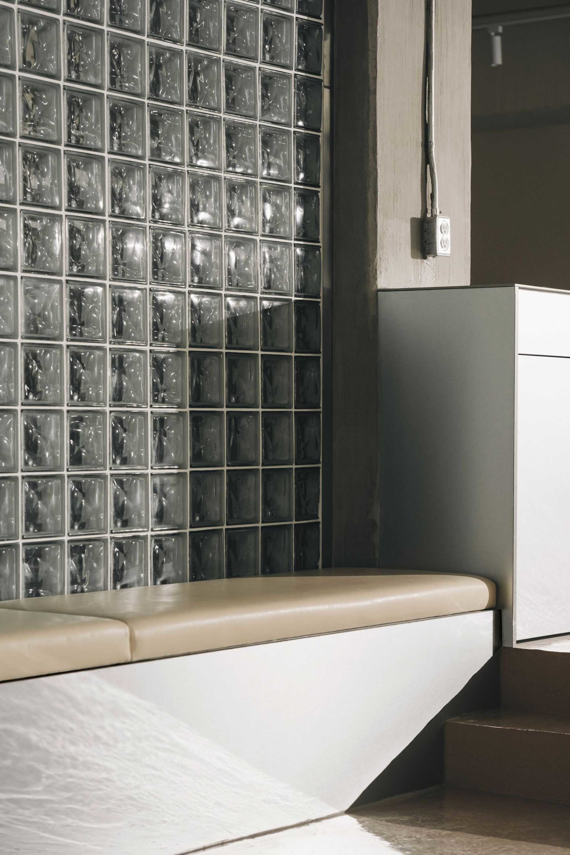A modern interior design featuring a glass and wood bench in front of a glass block wall, creating a calm and inviting atmosphere with a sense of openness