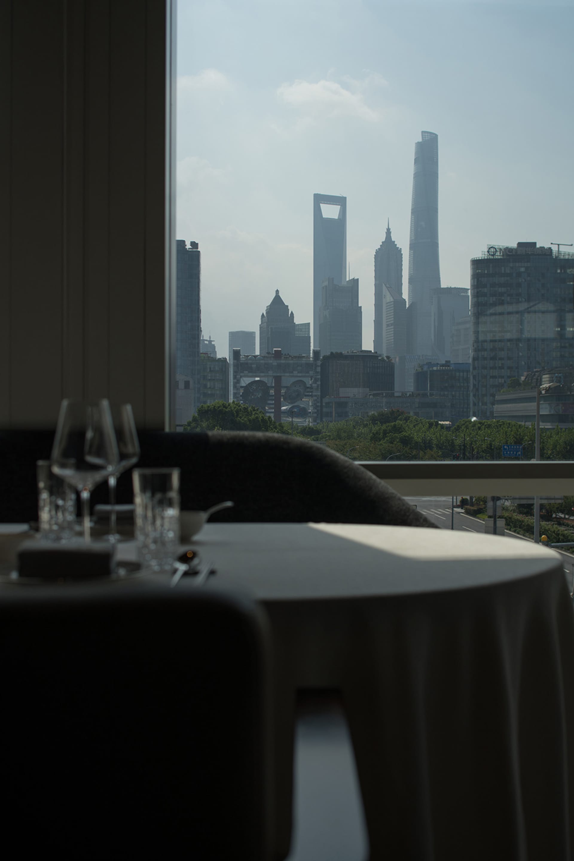 A rooftop dining space with a set table, wine glasses, and a city view from a high vantage point