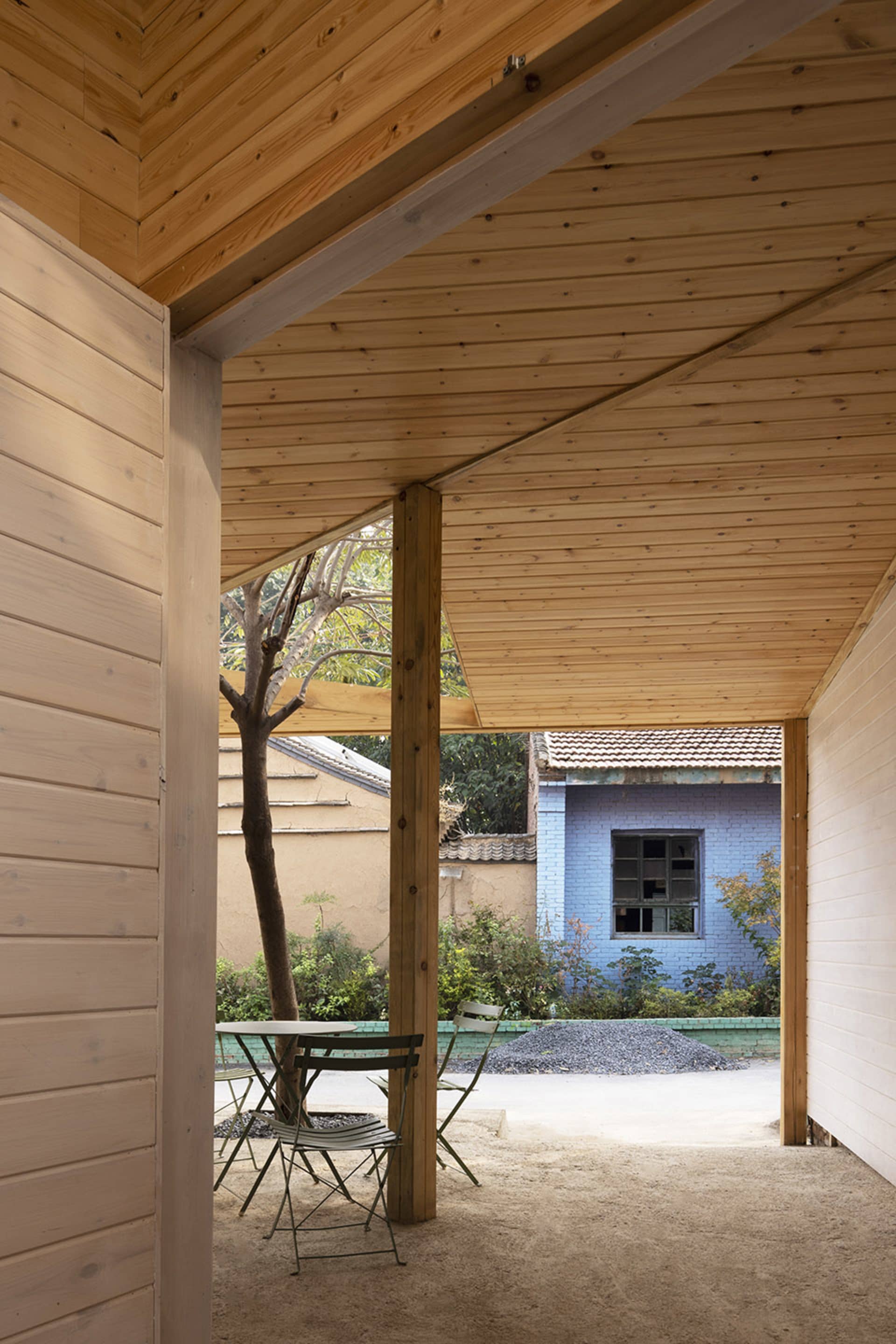 A calm and inviting outdoor patio with wooden walls, a green table, and two chairs, set in front of a blue building