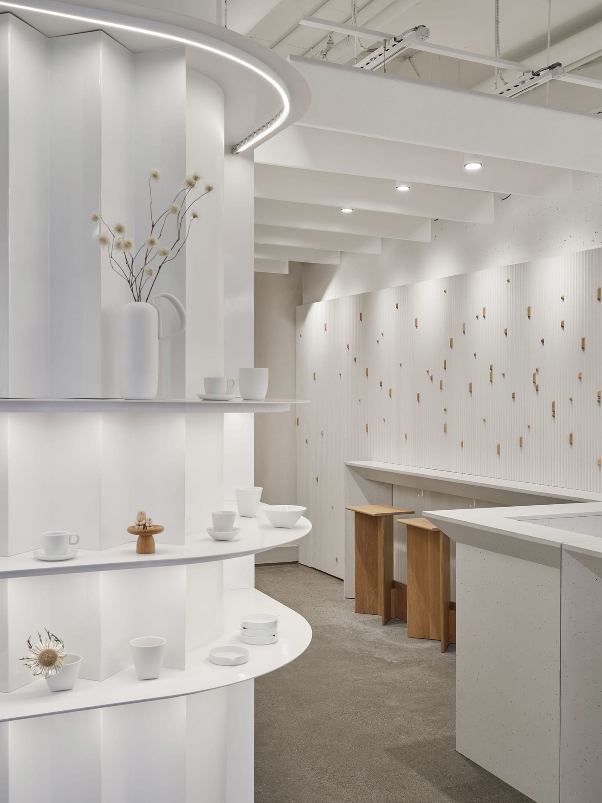 A well-lit kitchen showroom with white surfaces, a sink, countertop, and decorative items such as cups, bowls, vases, and potted plants