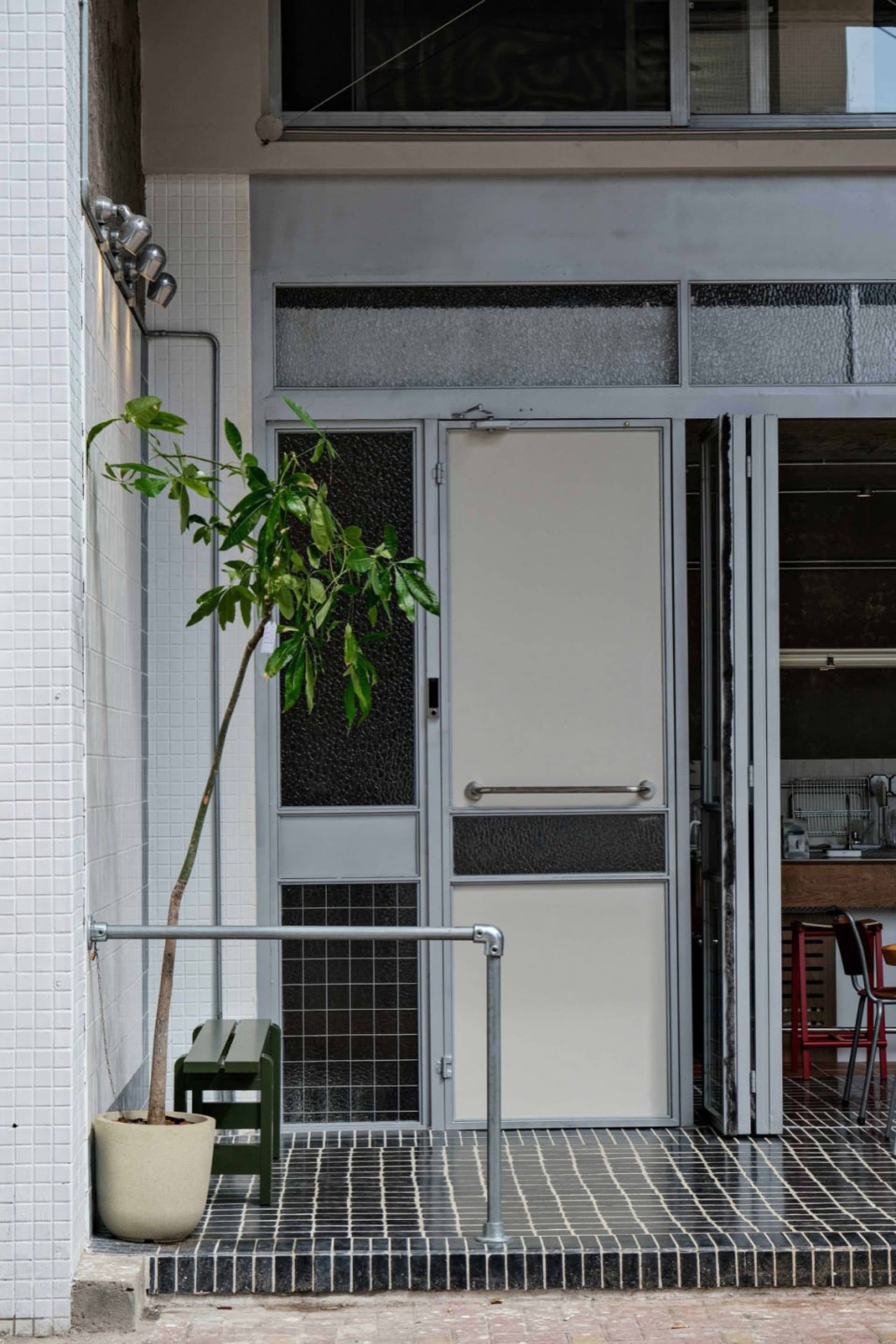 A modern entrance with a glass door, a bench, and two chairs in a residential space with a neutral color palette and natural light