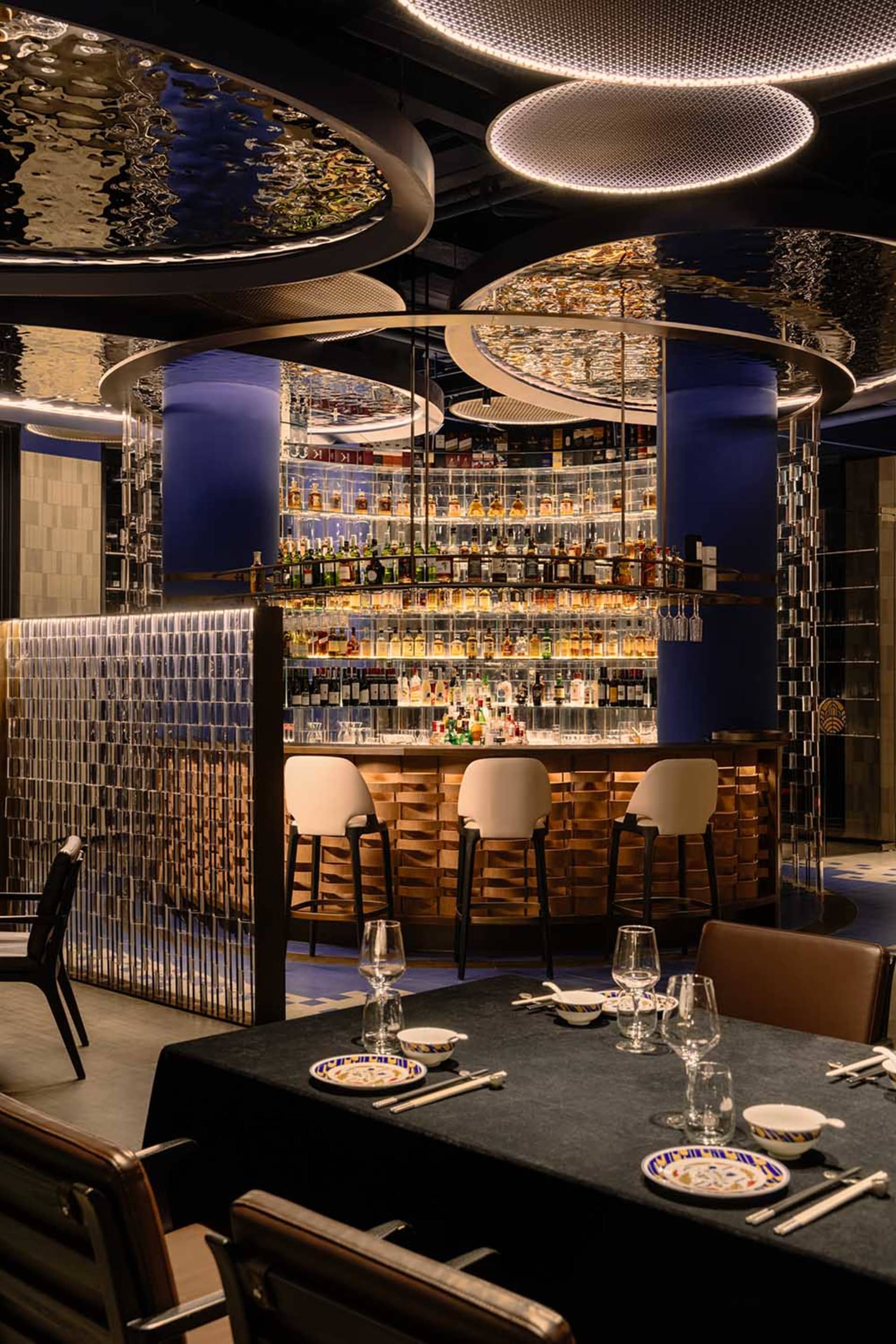 A cozy bar area with a large mirror behind the counter, surrounded by chairs and bottles on display