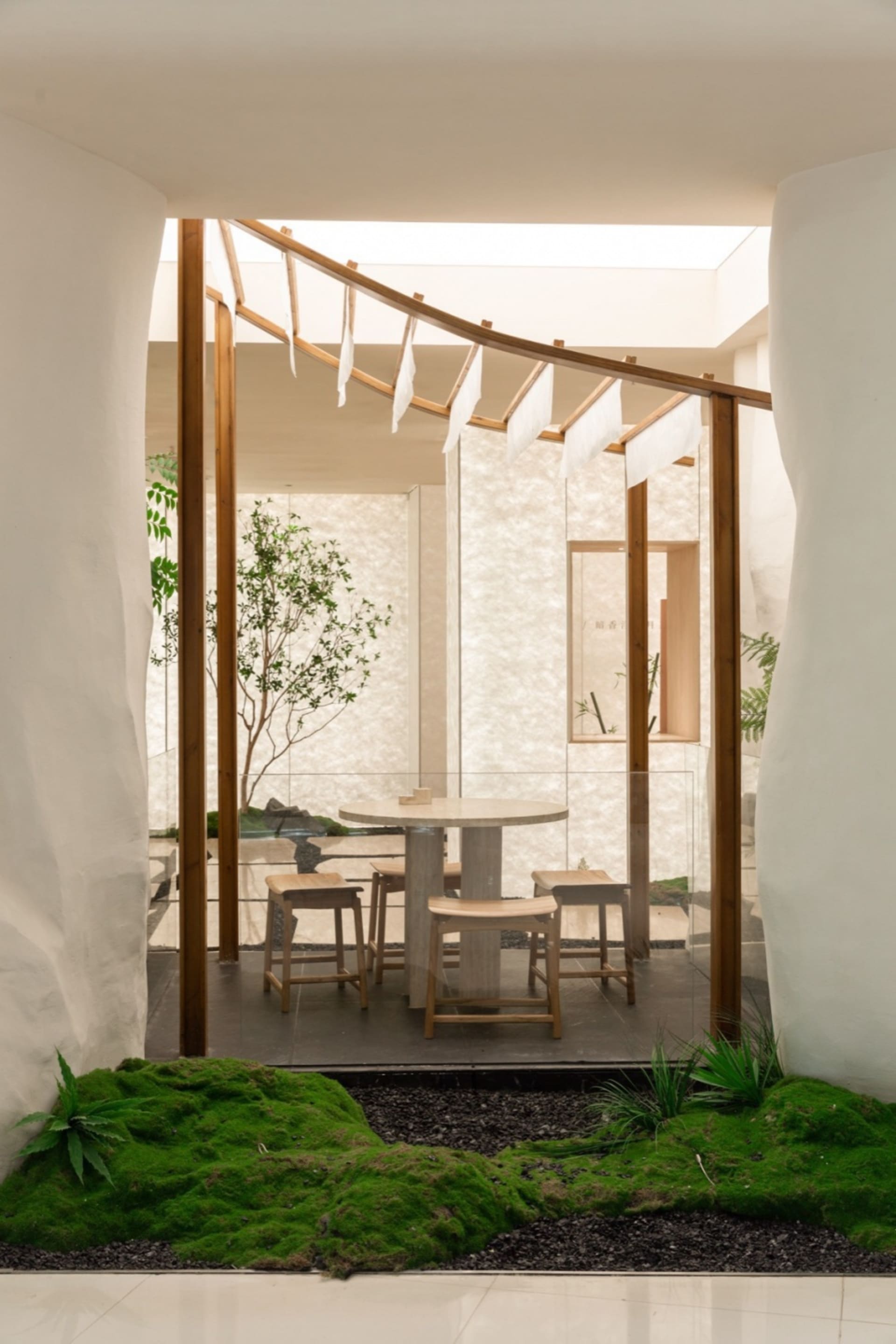 A modern dining area with a wooden table, glass top, and comfortable seating, surrounded by potted plants and a well-designed atmosphere