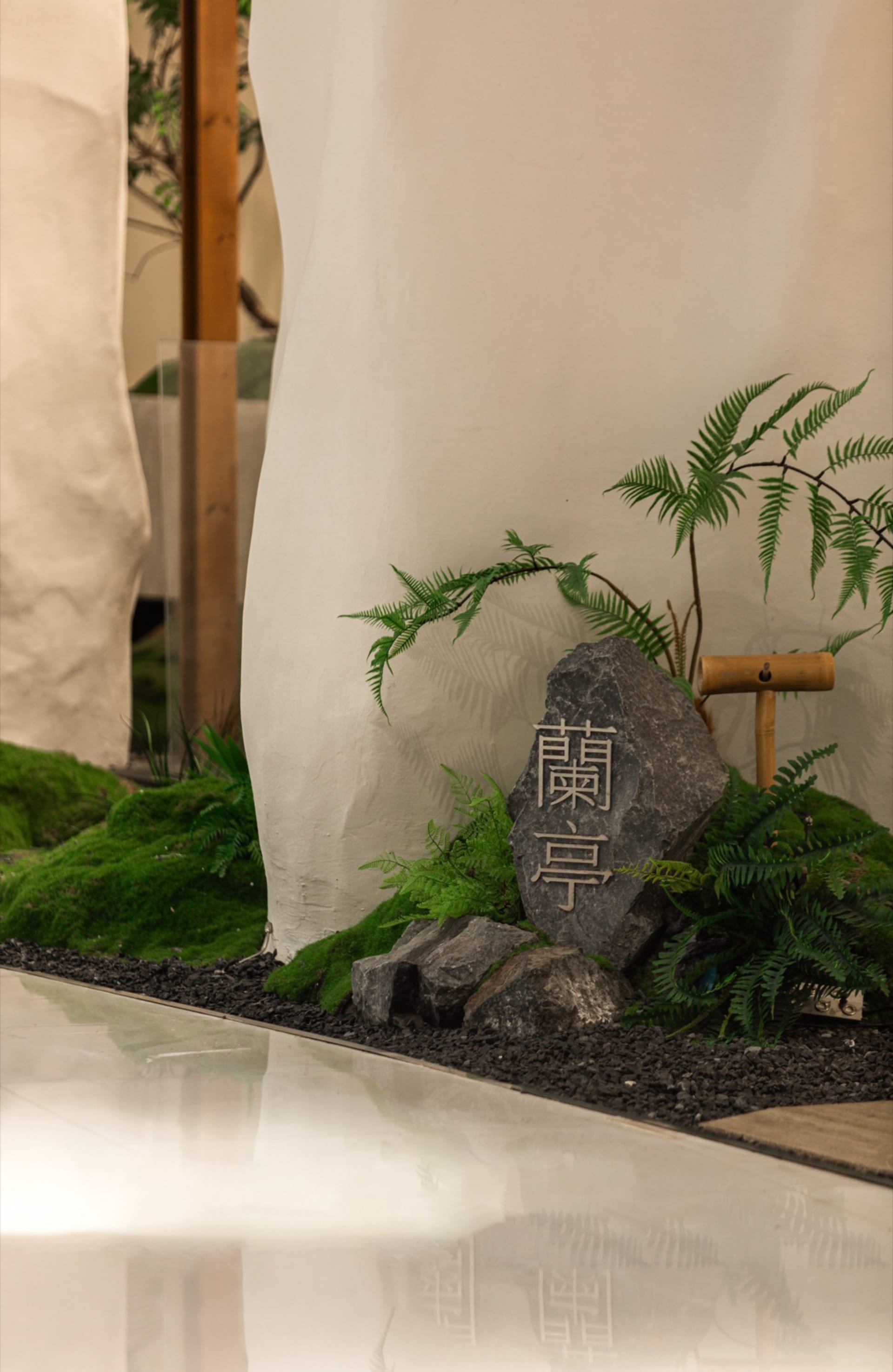 A serene indoor space with a stone wall, potted plants, and a bench, blending nature and architecture
